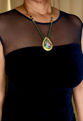 Model wearing evening dress with brass teardrop shaped dichroic glass pendant with a green beaded necklace. By 3D Glass Designs.
