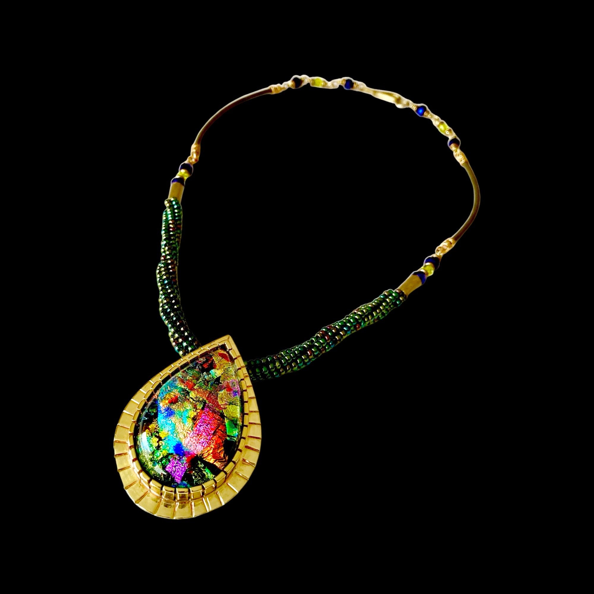 Handcrafted multicolor teardrop shaped dichroic glass, set in a custom-made brass setting, with a handmade seed bead and leather necklace. By 3D Glass Designs.