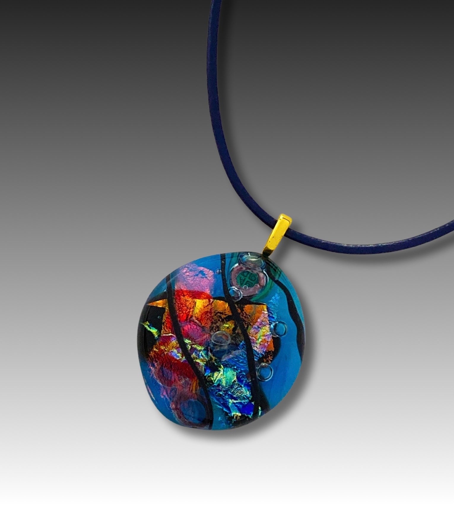 Fused glass pendant on a blue leather cord. Transparent blue glass with layers of red, rust, blue, green and purple dichroic glass and a copper squiggle design embedded in the glass. By 3D Glass Designs