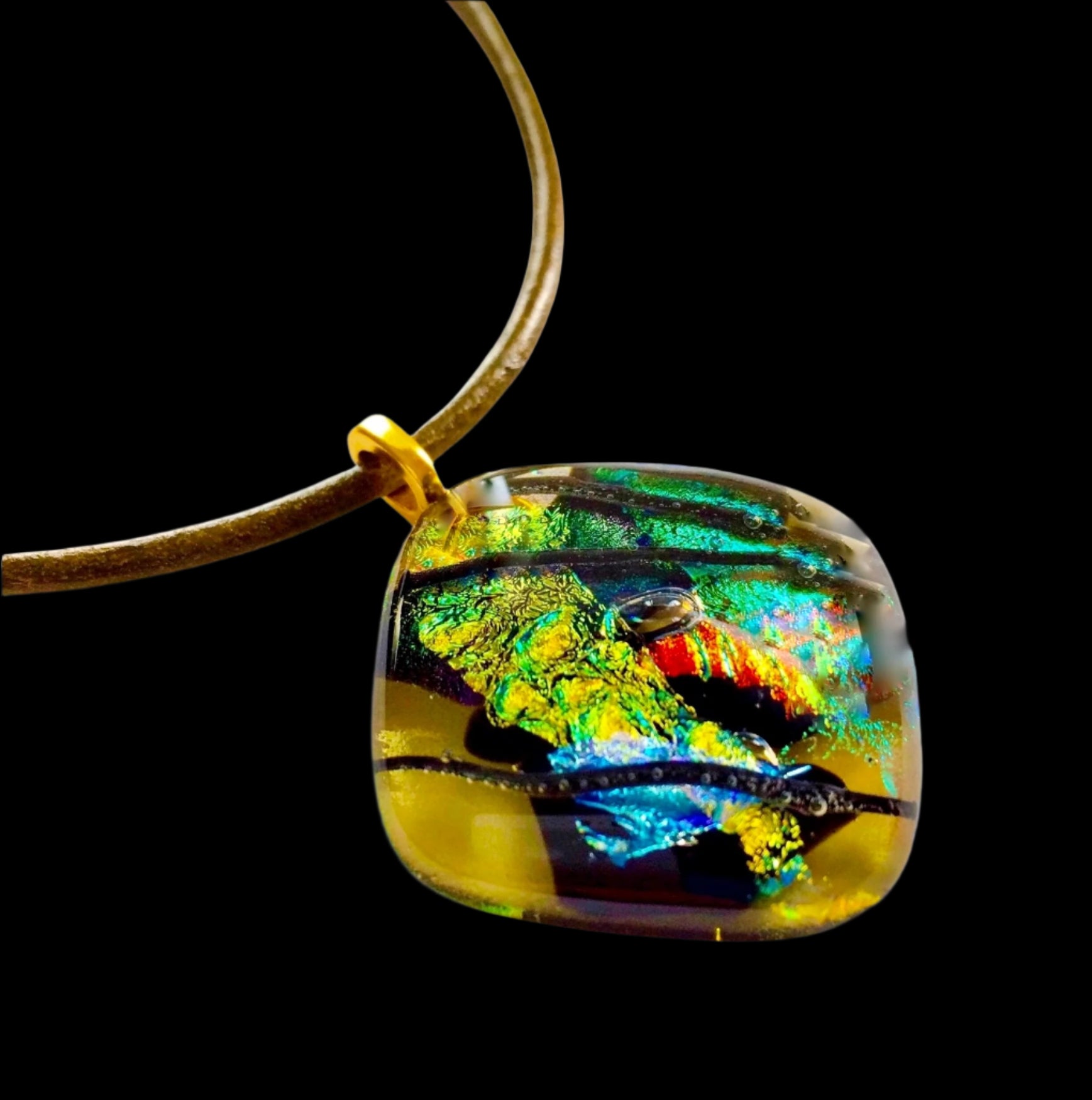 Fused glass pendant in transparent yellow with red, blue, green, purple and gold dichroic glass. Streaks of black add contrast to the design. Diamond shaped pendant hangs on an olive-green leather cord, by 3D Glass Designs.