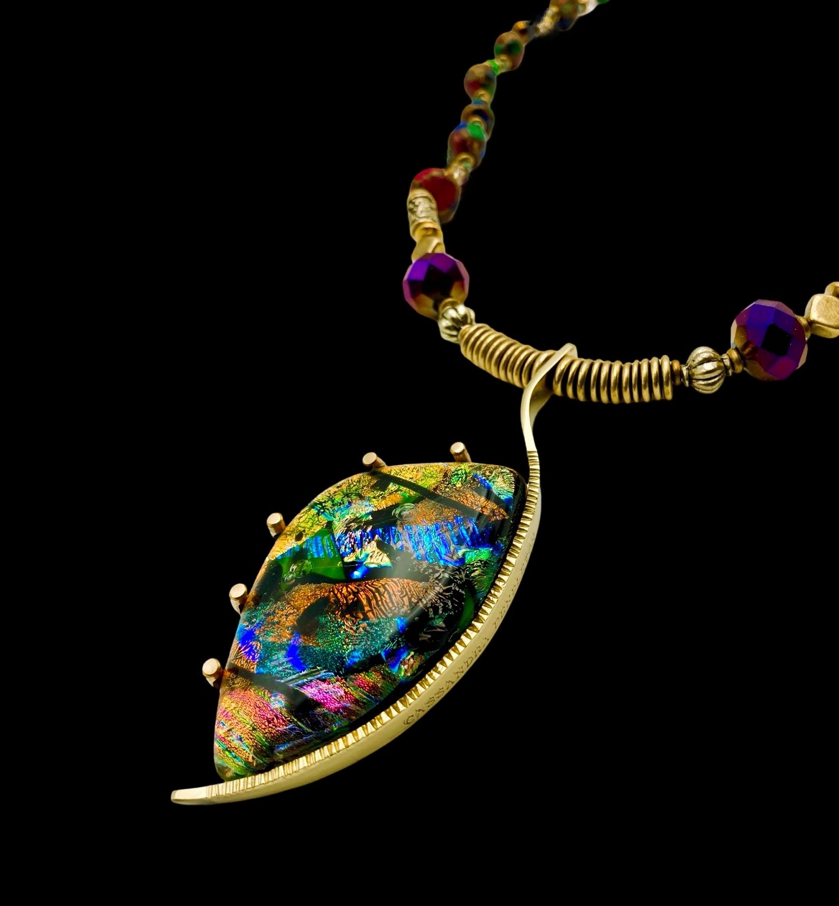 Dichroic glass set in a unique brass pendant, with prongs on left side and a textured bezel on the right side. Pendant is hung on a 29" long hand-knotted multicolor beaded necklace, by 3D Glass Designs.