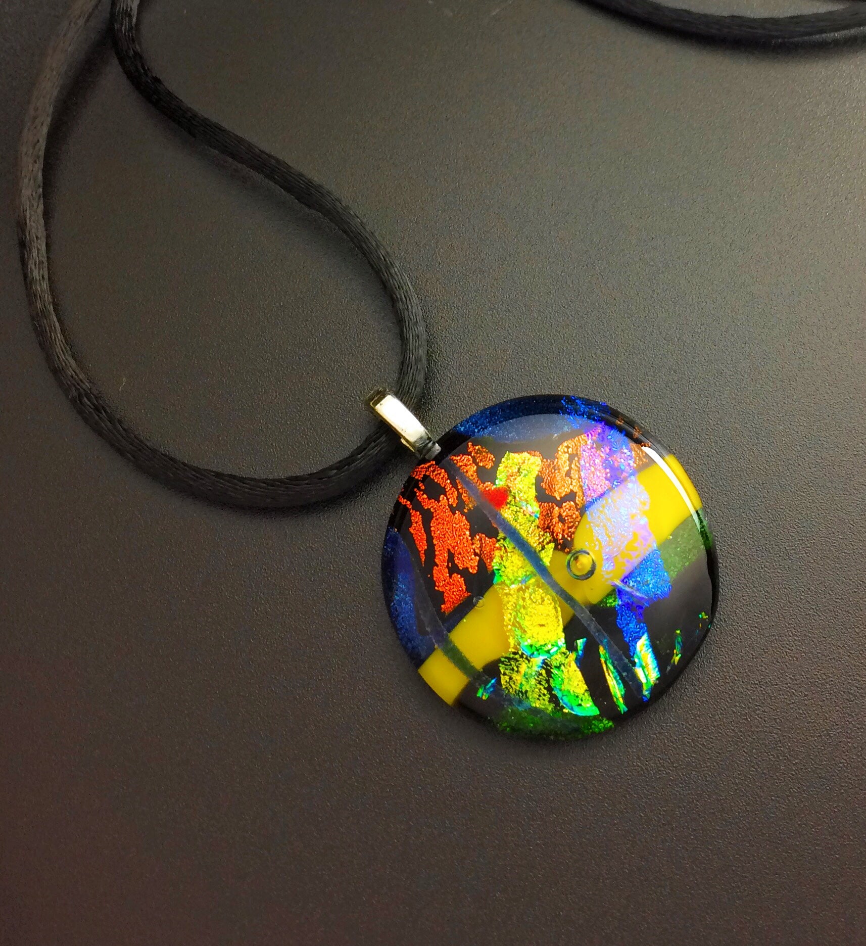 Round dichroic glass pendant necklace in green, yellow, blue, and rust hung on a 16-inch satin cord, by 3D Glass Designs.