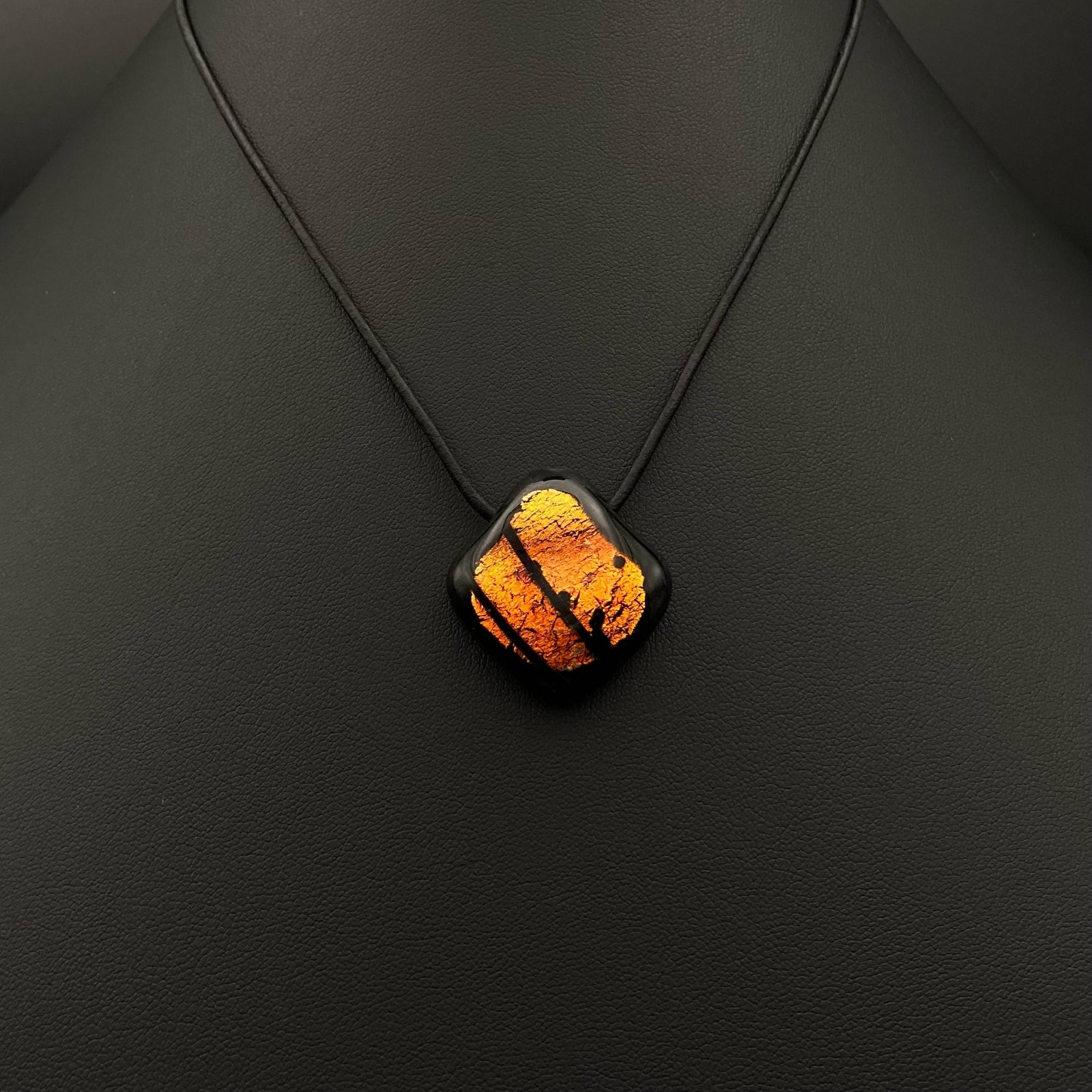 Orange and black fused glass pendant on a black leather cord against a black leather background, by 3D Glass Designs.