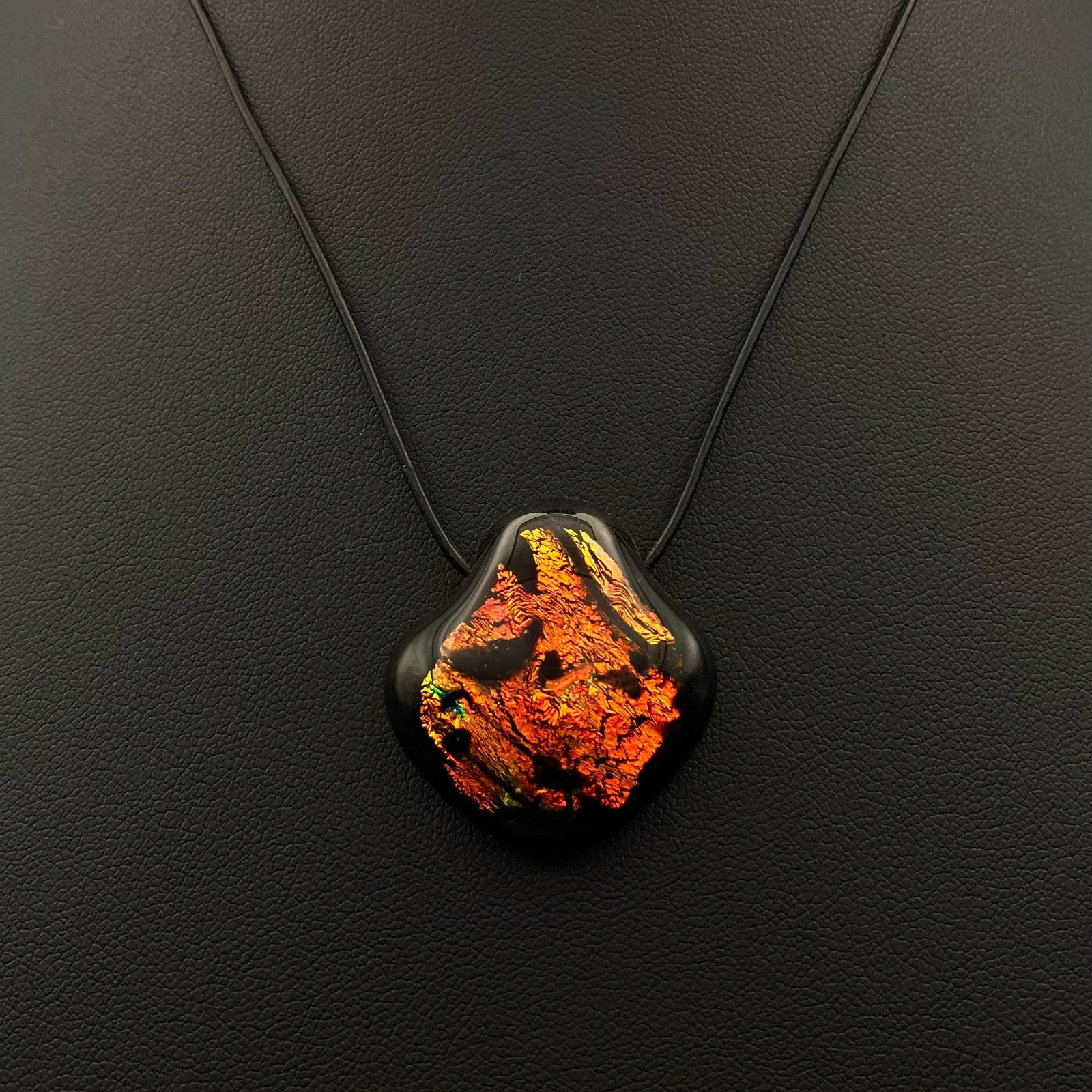 Orange and black pendant on a black leather cord against a black background, by 3D Glass Designs.