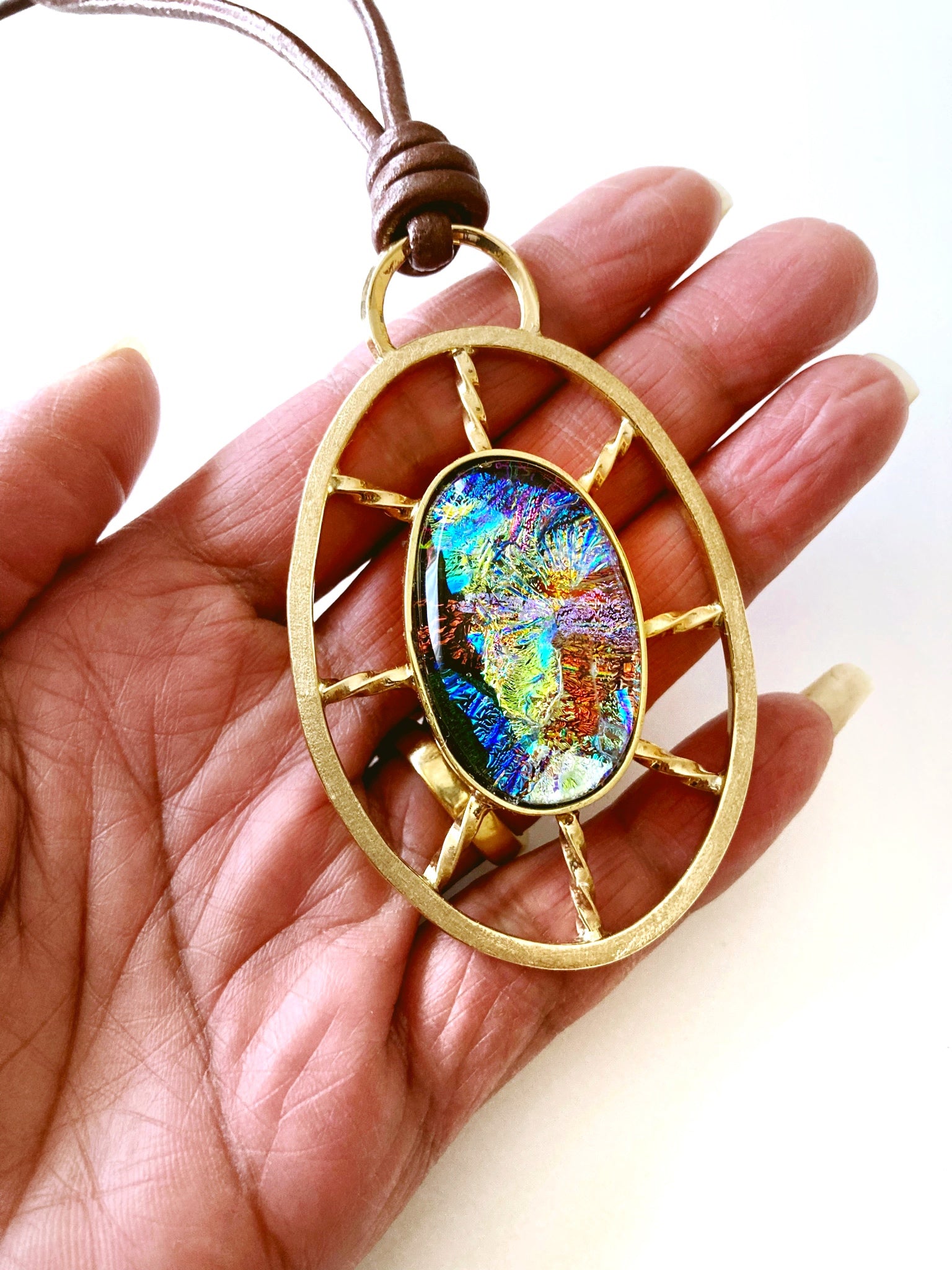 Models' hand holding fused glass set in a nautical wheel shaped brass pendant setting, by 3D Glass Designs.