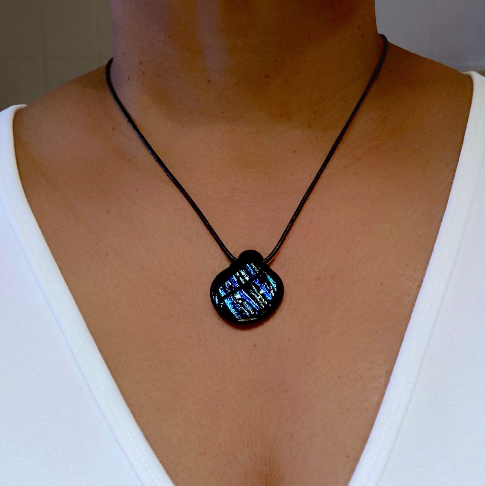 Model wearing blue striped glass pendant on a black leather cord, by 3D Glass Designs.