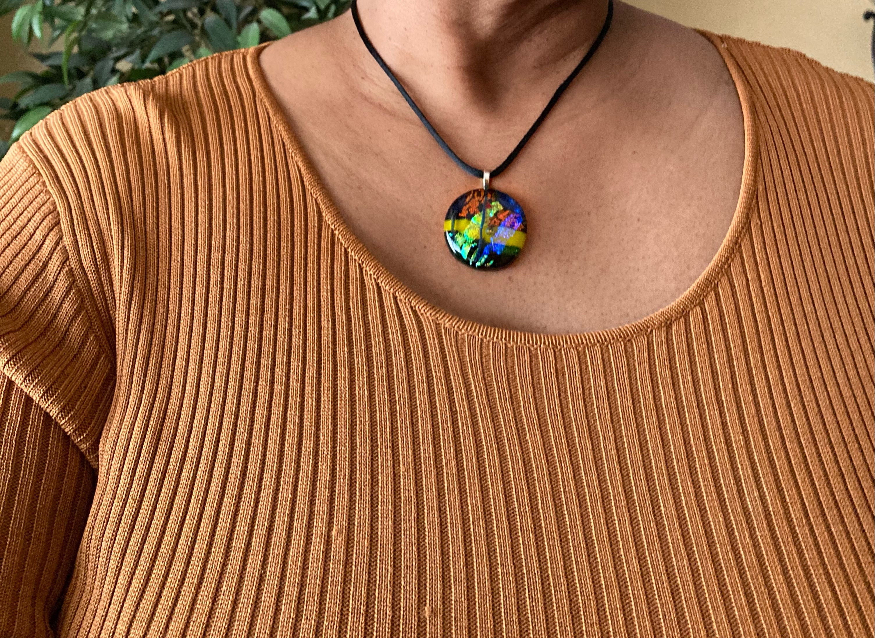 Model wearing round fused glass pendant necklace in green, yellow, blue, and rust hung on a 16-inch satin cord, by 3D Glass Designs.