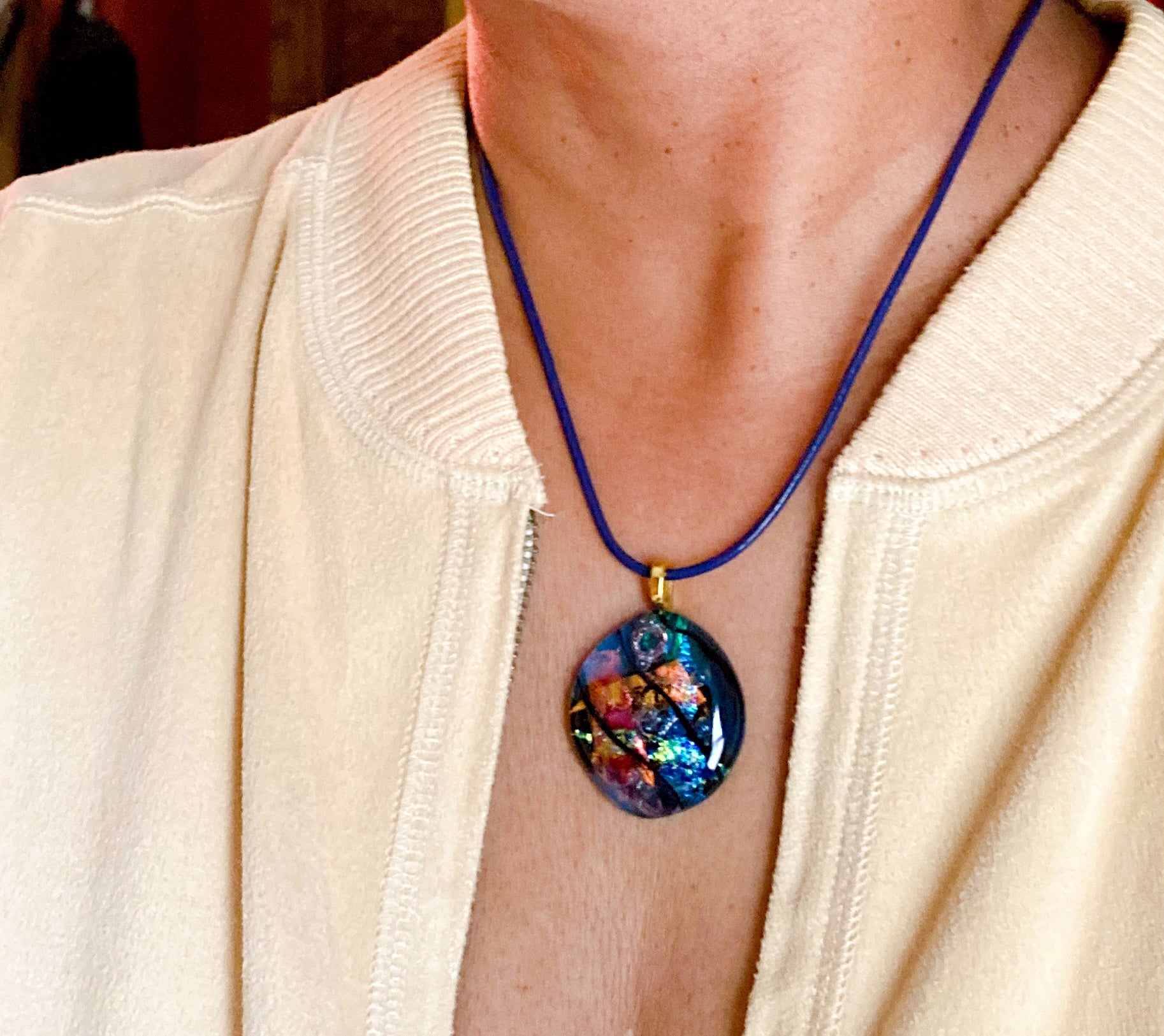 Fused glass pendant on a blue leather cord. Transparent blue glass with layers of red, rust, blue, green and purple dichroic glass and a copper squiggle design embedded in the glass. By 3D Glass Designs