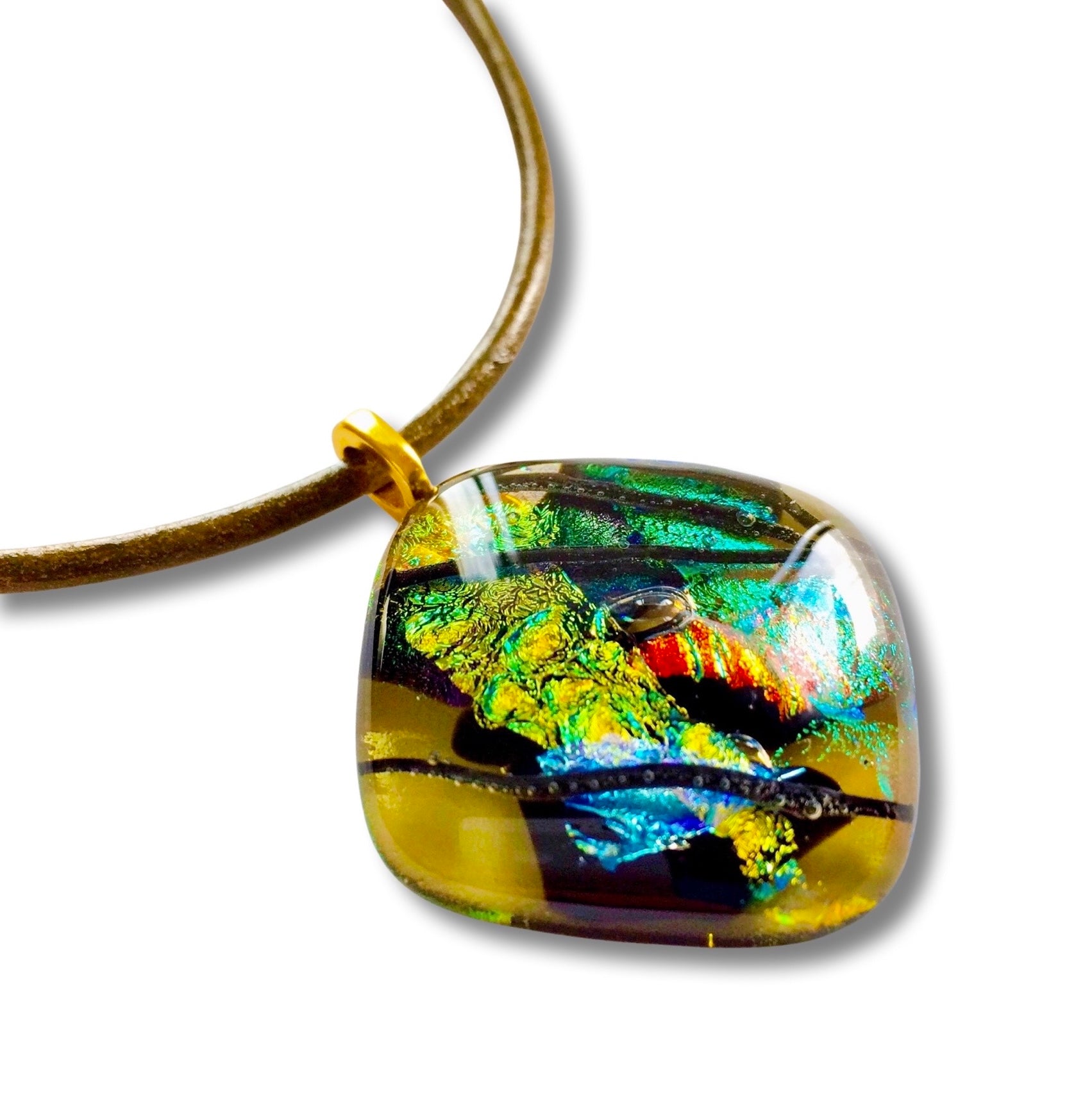 Fused glass pendant in transparent yellow with red, blue, green, purple and gold dichroic glass. Streaks of black add contrast to the design. Diamond shaped pendant hangs on an olive-green leather cord, by 3D Glass Designs.