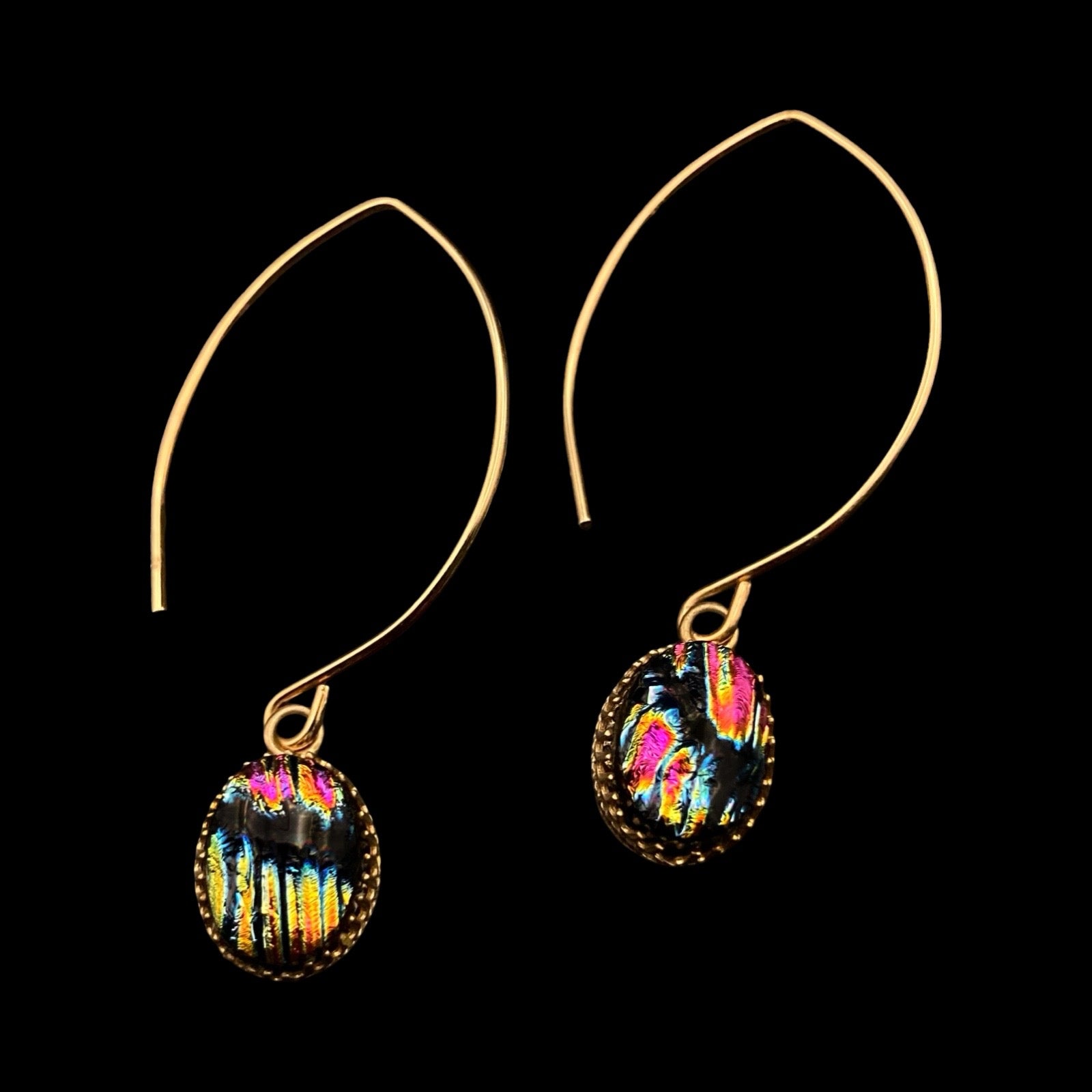 A pair of pierced earrings with multi-colored dichroic glass drops on long gold-plated ear wires against a black background, by 3D Glass Designs.
