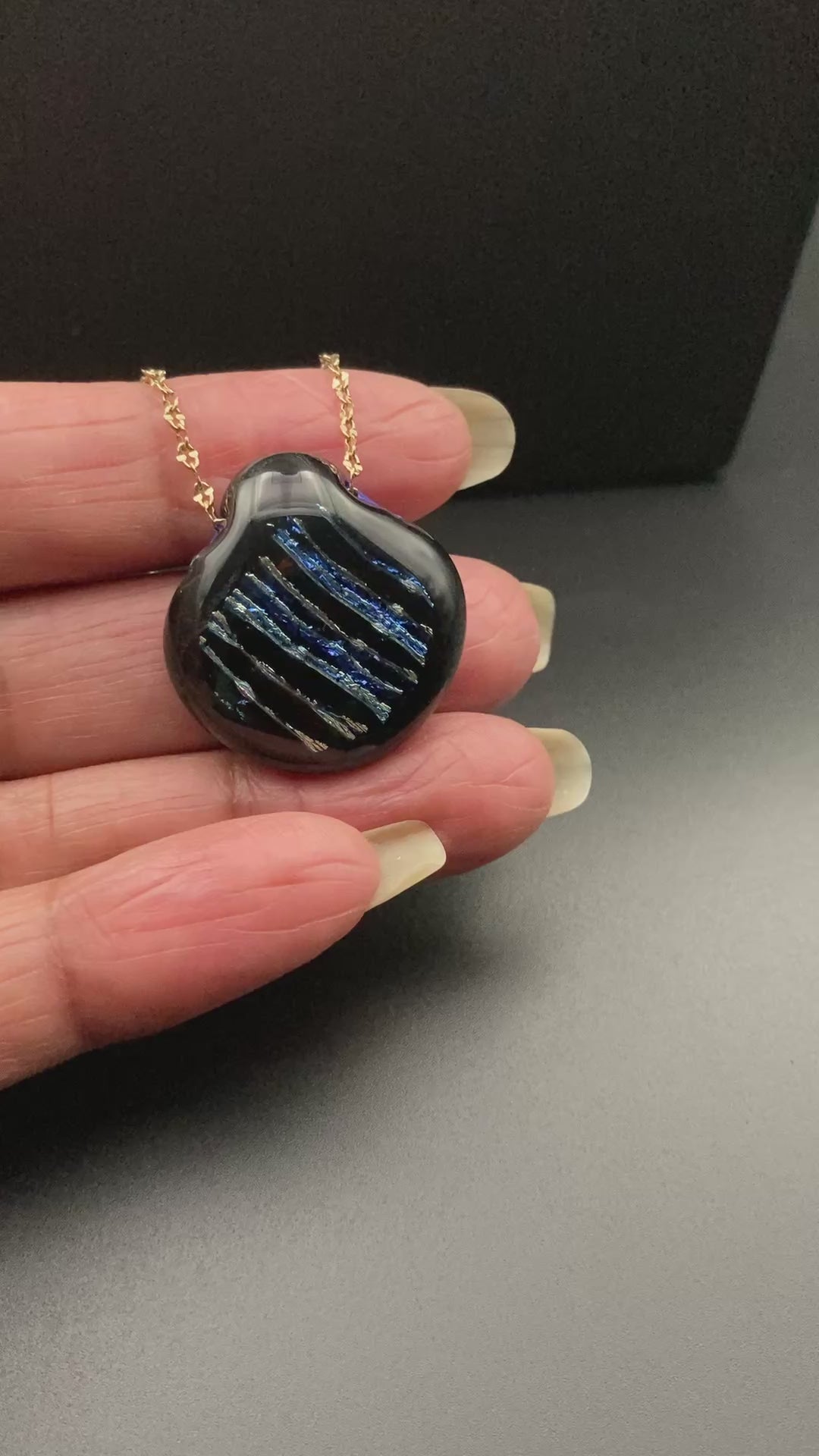 Hand holding dichroic glass pendant on a delicate chain, by 3D Glass Designs.