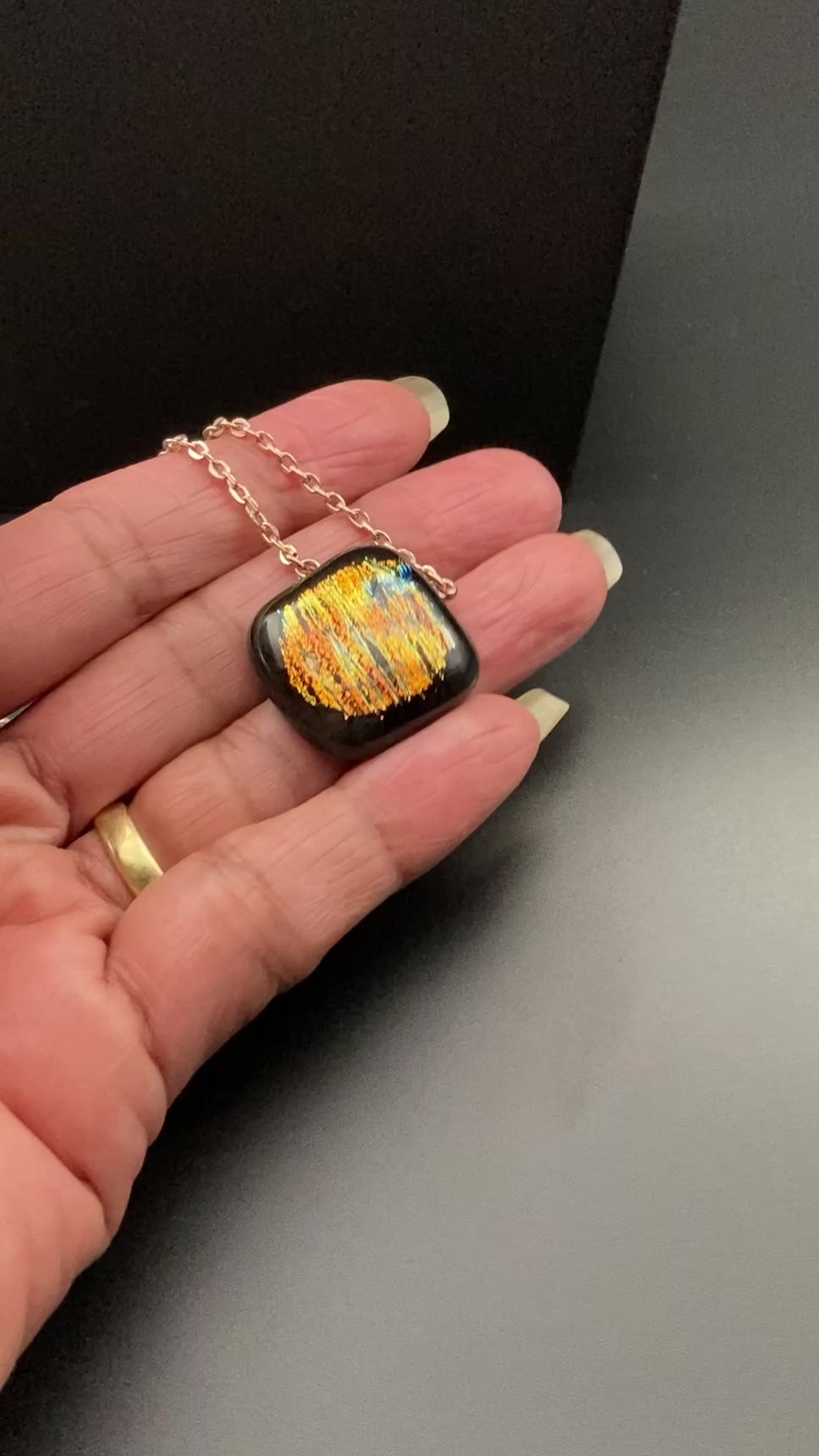 Hand holding orange dichroic glass pendant, by 3D Glass Designs.
