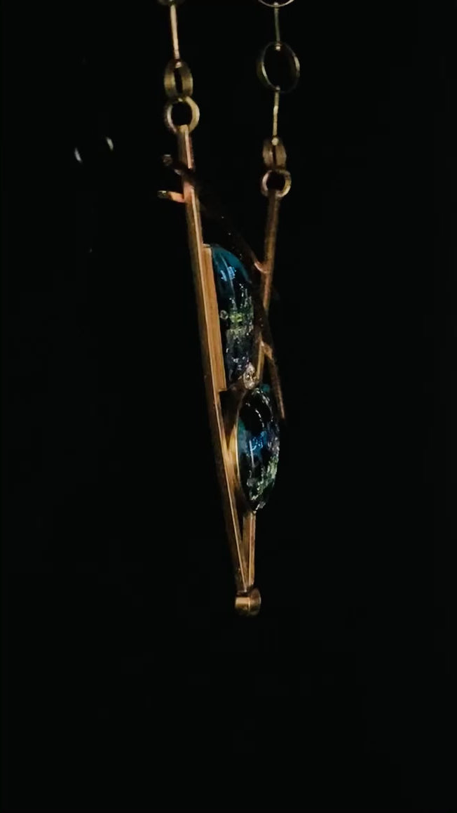 Video of geometric inspired brass and teal fused glass pendant necklace. Large statement pendant with two glass semi-circles with a CZ in between, set in a V frame with two slightly cured arch's above. Chain has various sized brass circles linked together, by 3D Glass Designs.