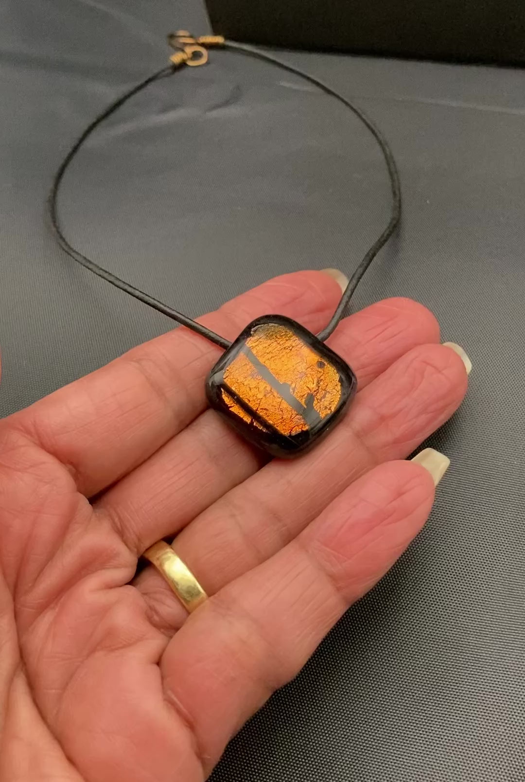 Hand holding orange and black fused glass pendant against a dark cloth background, by 3D Glass Designs.