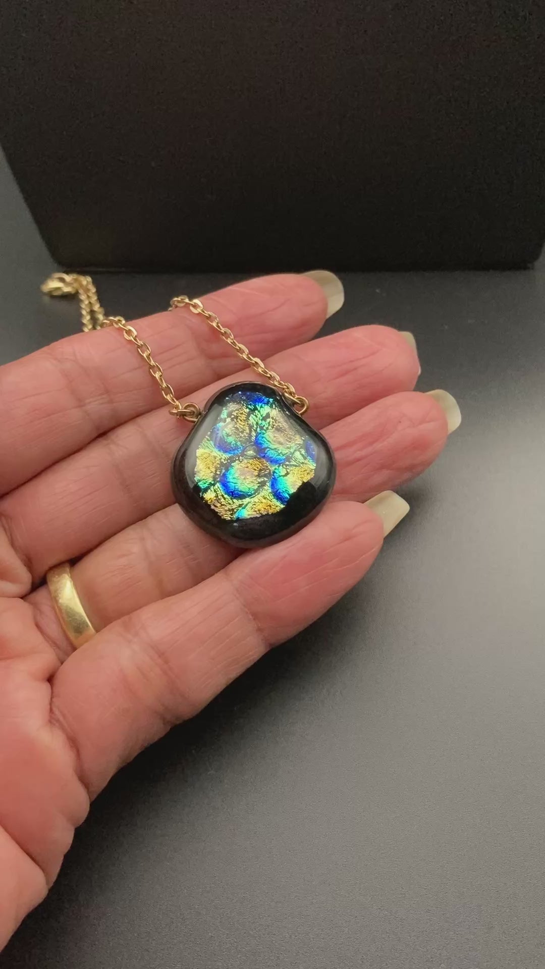 Hand holding a glass pendant with a gold chain, by 3D Glass Designs.