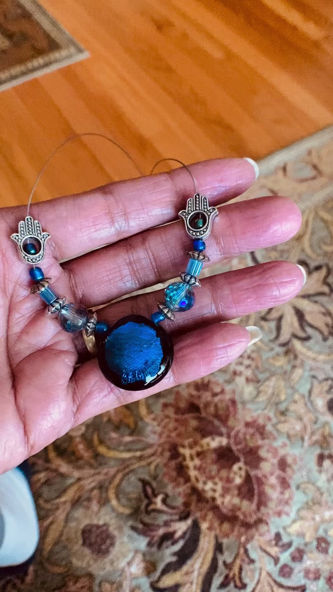 Hand holding beaded necklace with a floral rug and hardwood floor as the background.