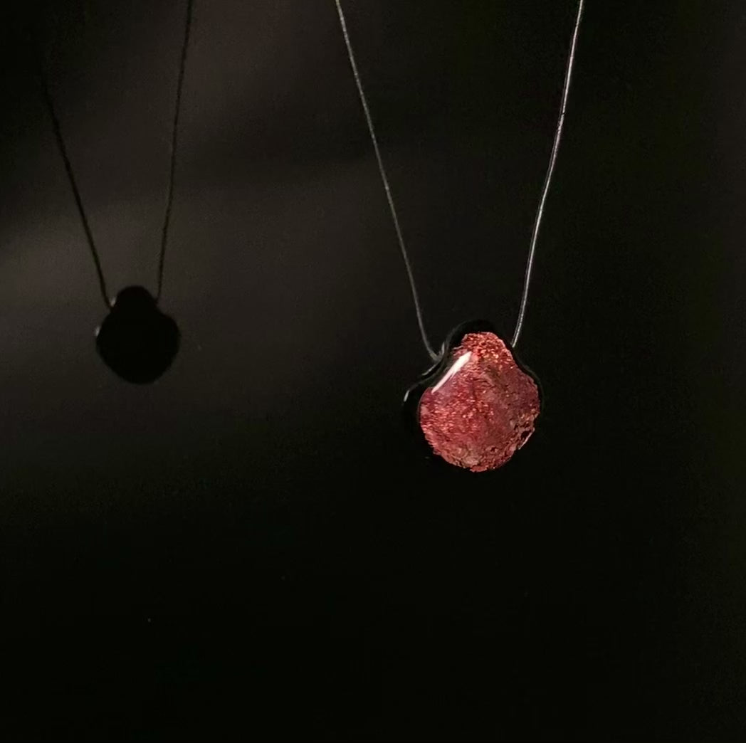 Dichroic glass pendant rotating against a shiny black background with its reflection on the left, by 3D Glass Designs.