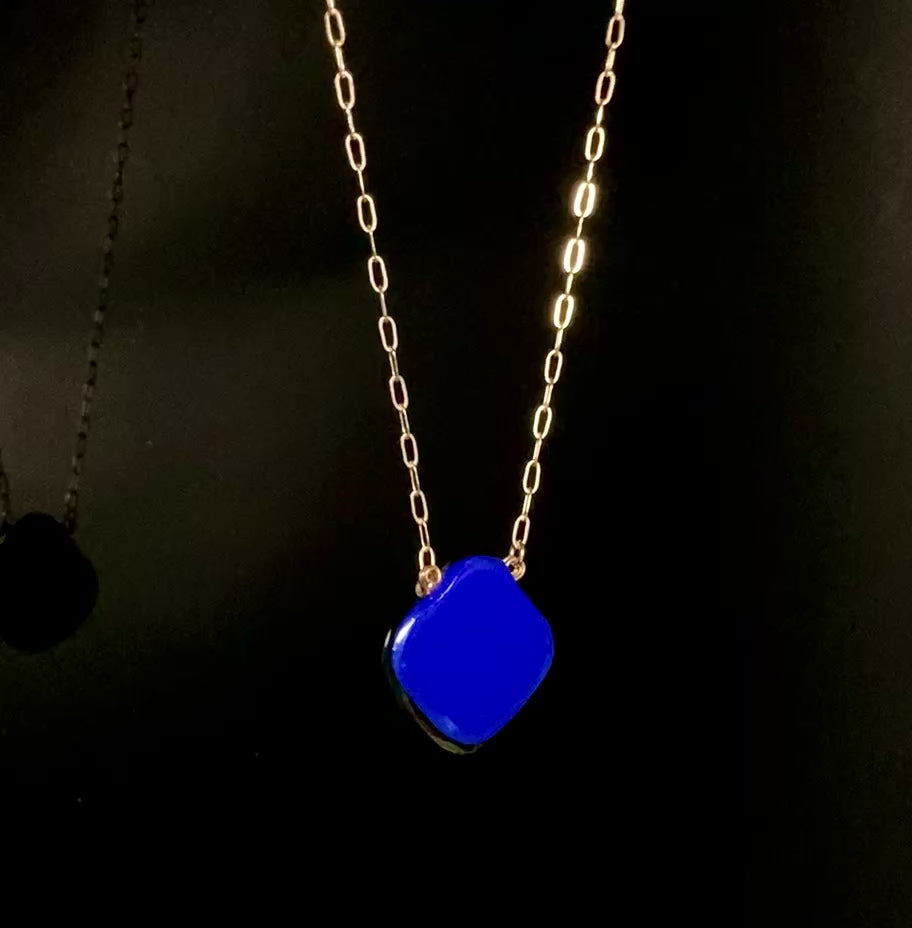 Rotating dichroic glass pendant on a gold chain against a black background, by 3D Glass Designs.