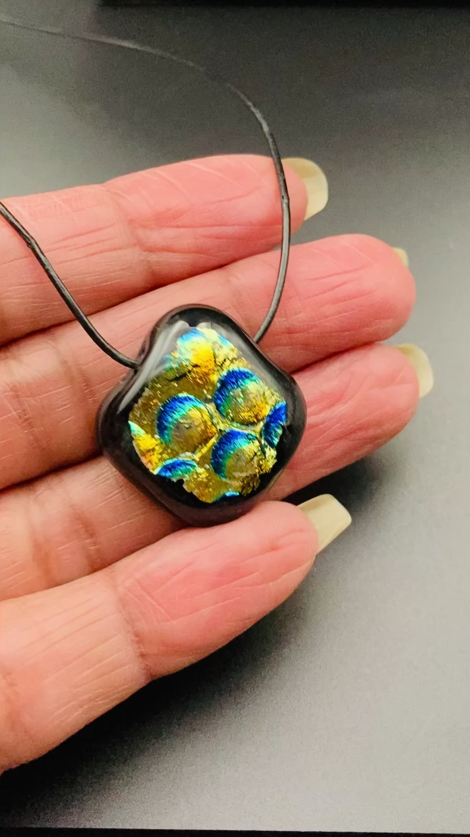 Hand holding a small, fused glass pendant, by 3D Glass Designs.
