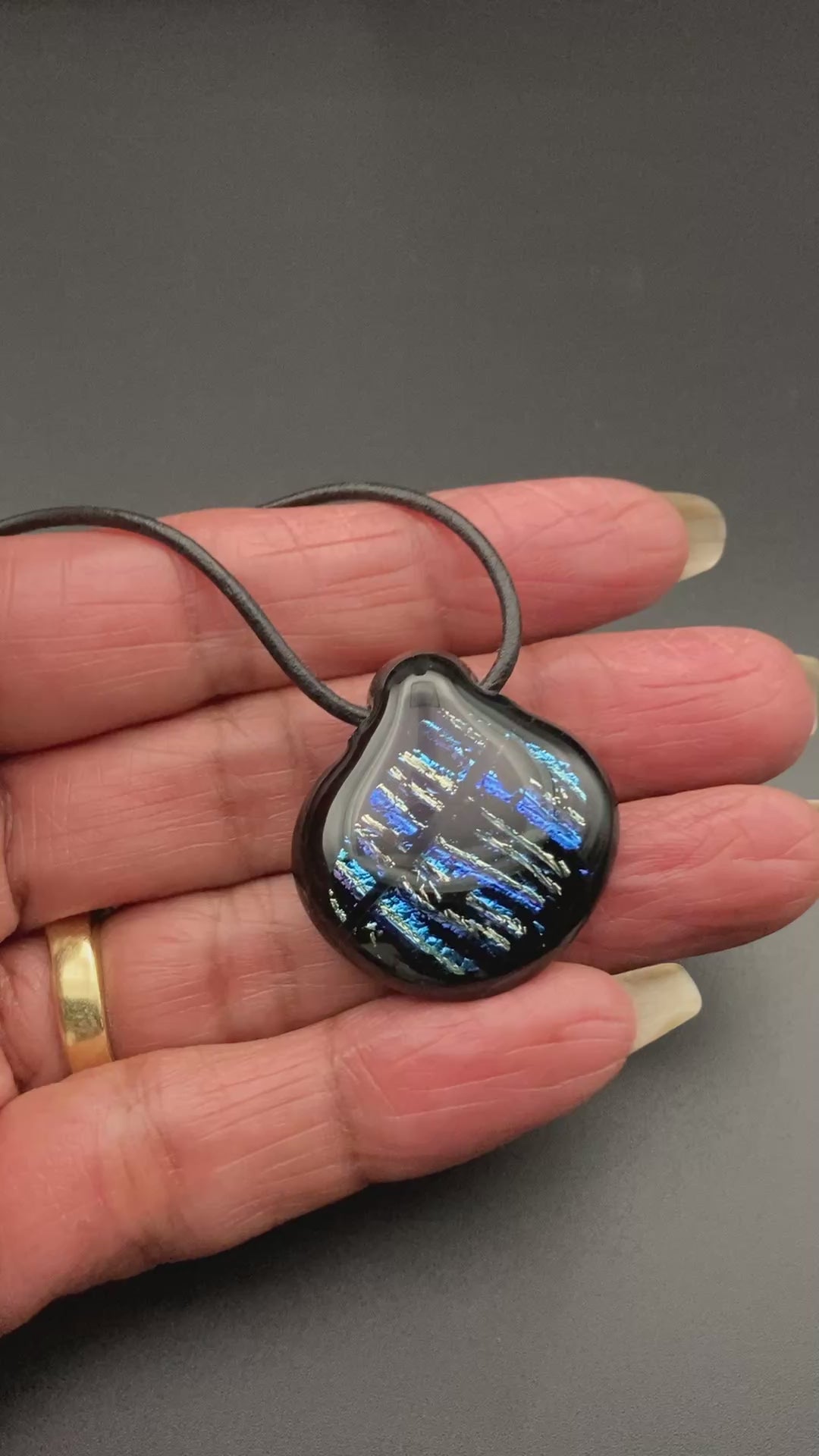 Hand holding black and blue dichroic glass pendant, by 3D Glass Designs.