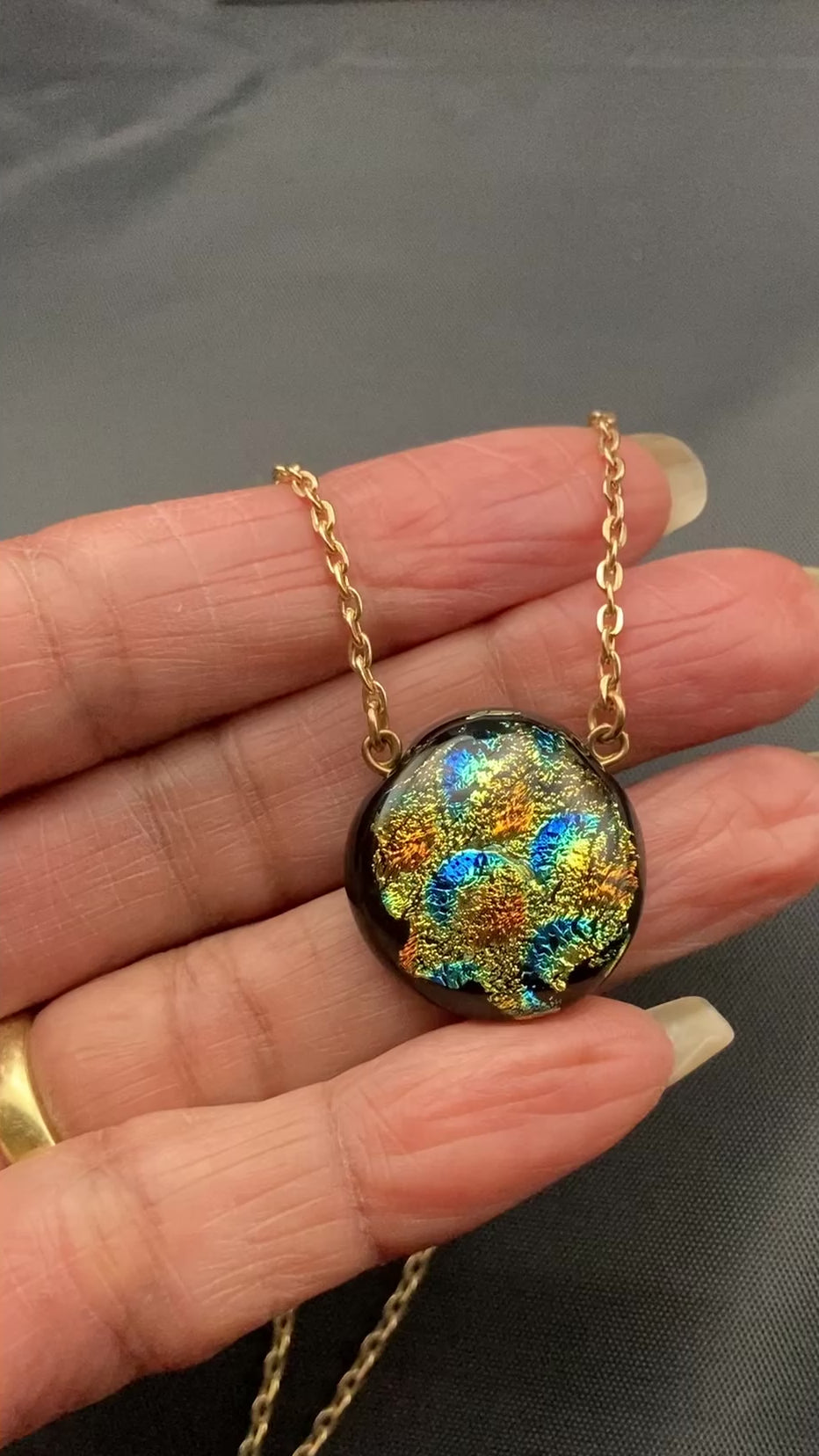 Hand holding small round glass pendant on gold chain, by 3D Glass Designs.