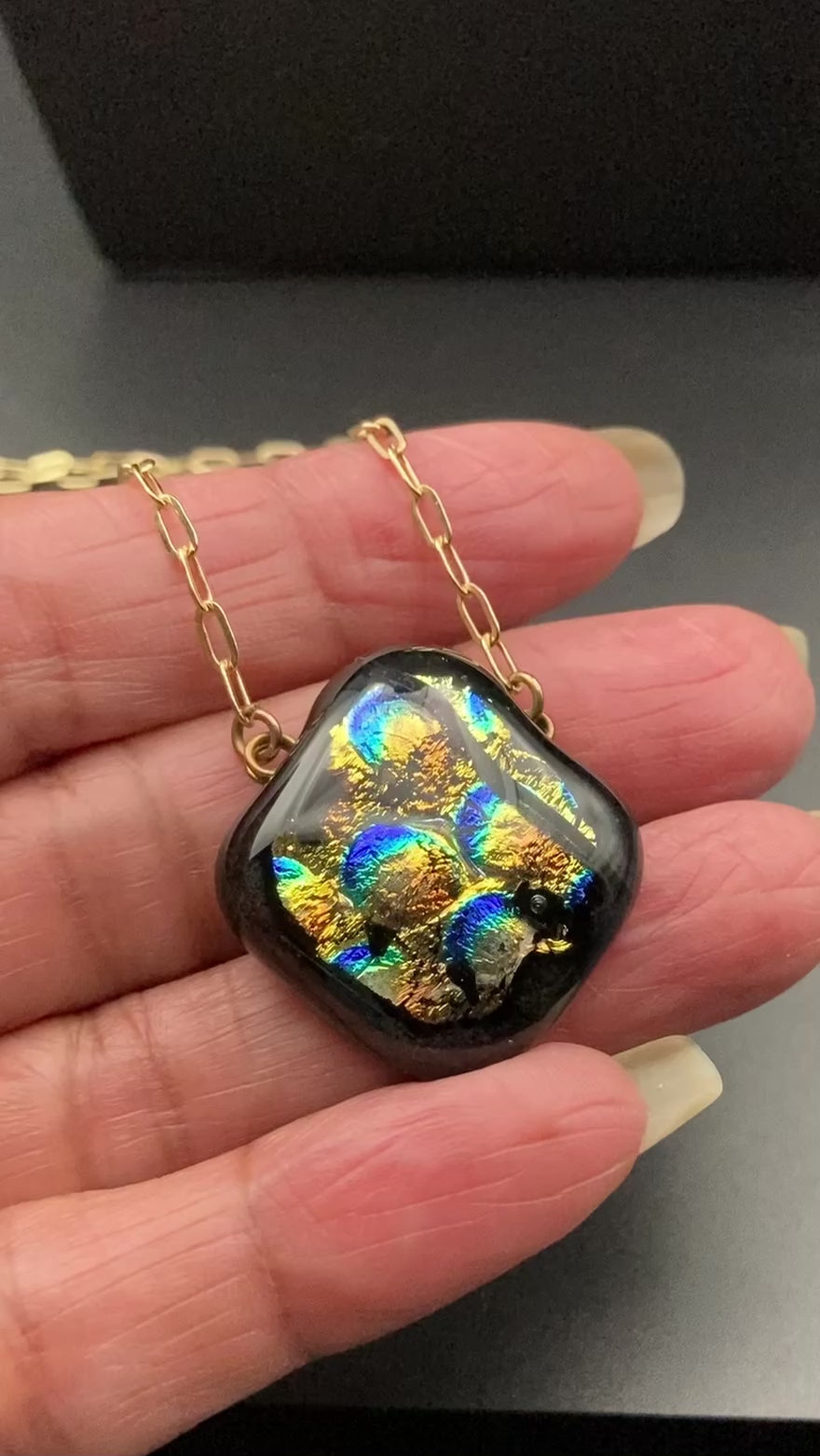 Hand holding dichroic glass pendant, by 3D Glass Designs.
