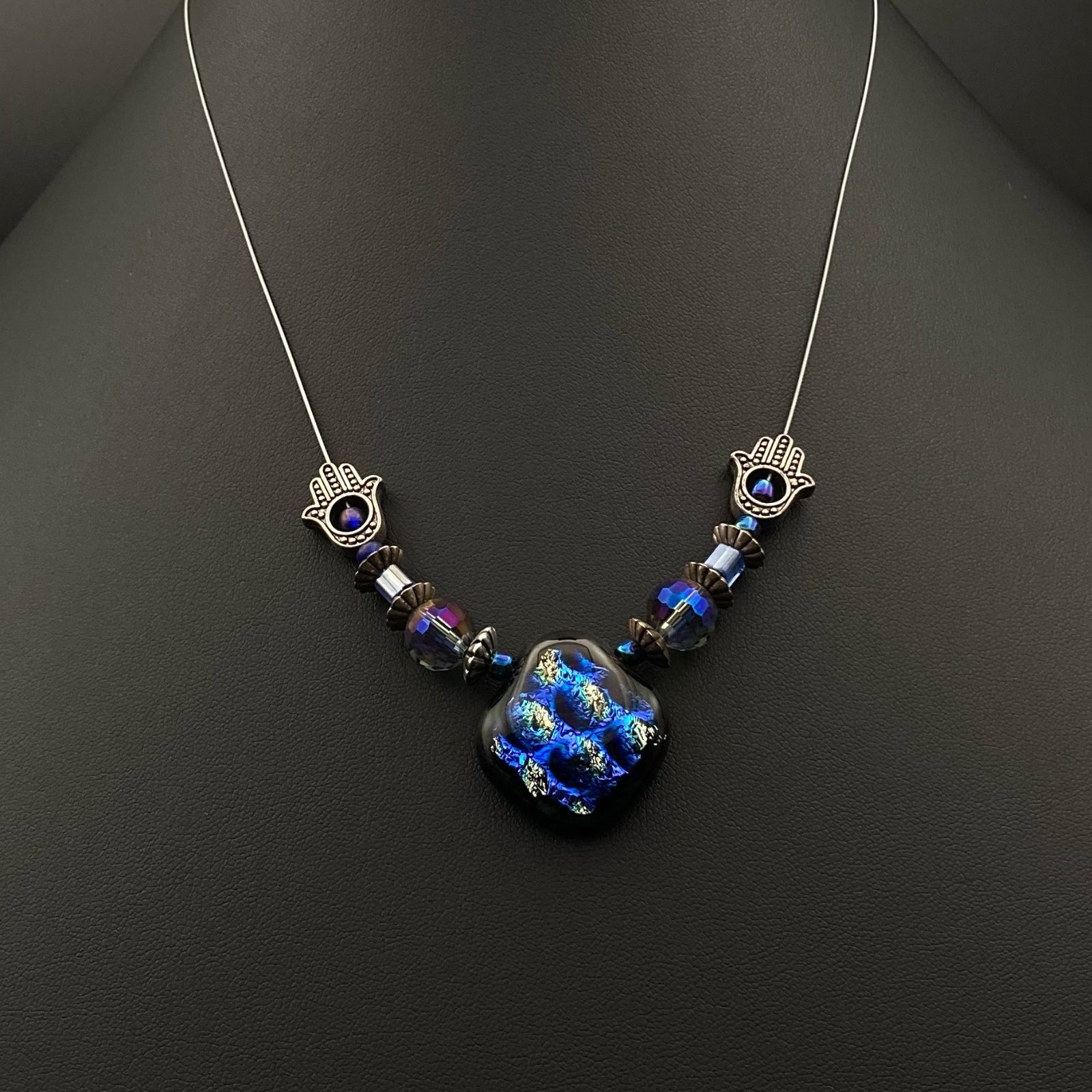 Beaded pendant necklace on a silver cord against a dark leather background, by 3D Glass Designs.
