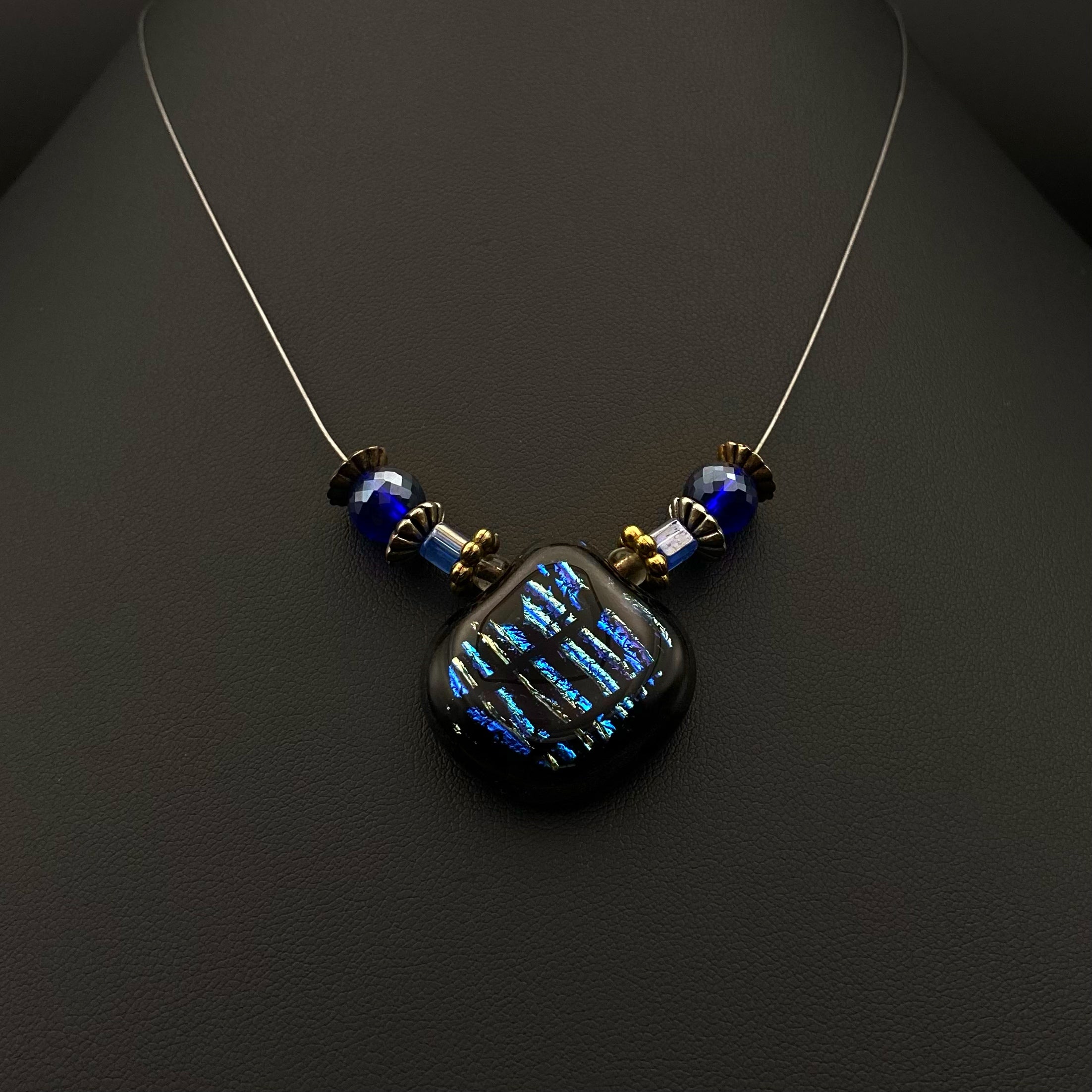 Beaded necklace with blue striped dichroic glass pendant against a black background, by 3D Glass Designs.