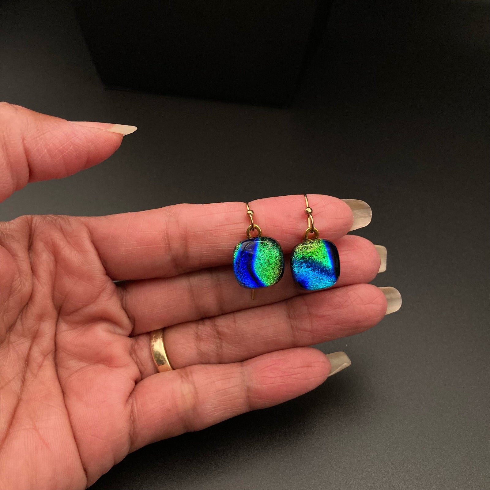 Hand holding a pair of blue-green glass earrings, by 3D Glass Designs.