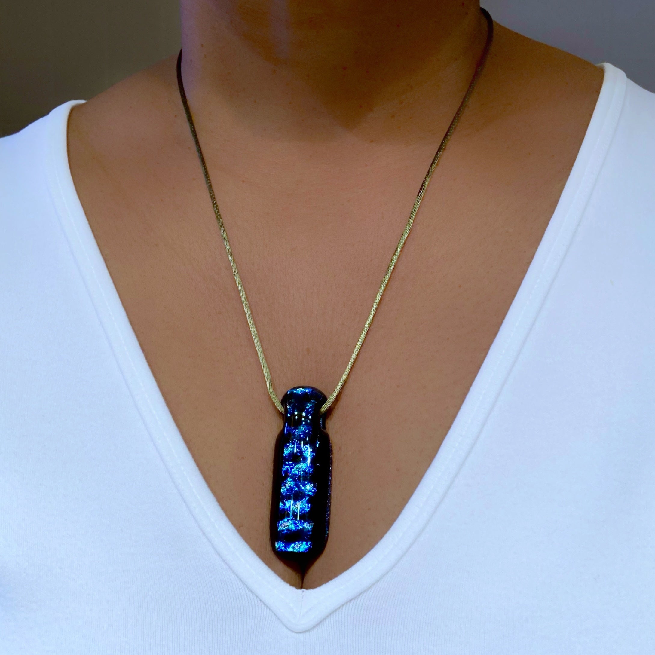 Model wearing long fused glass pendant and a white shirt.