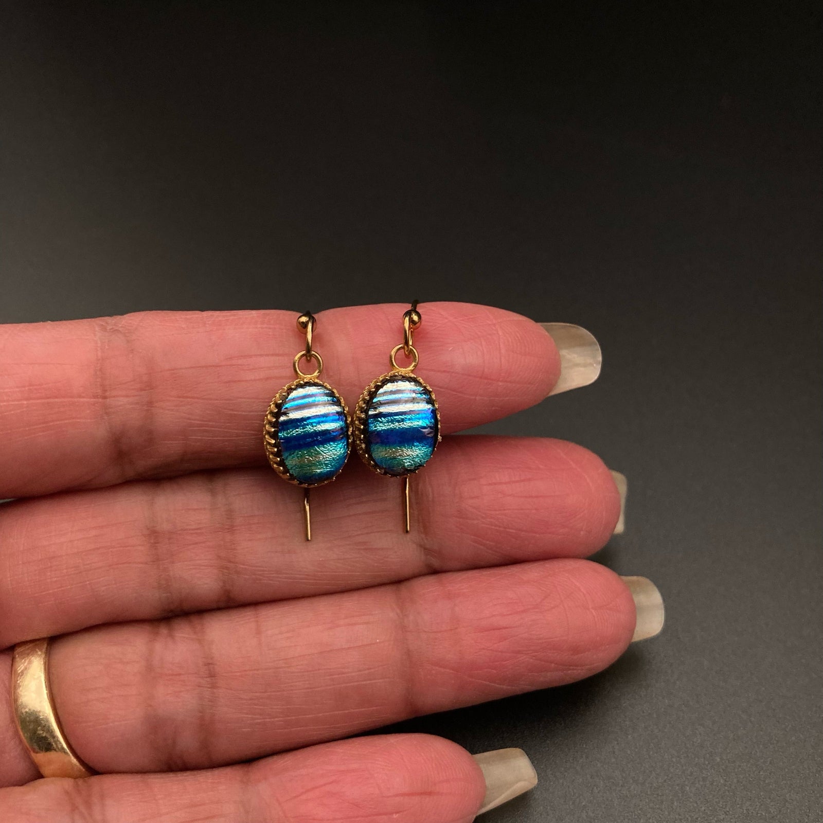 Hand holding a pair of dainty blue striped glass earrings, by 3D Glass designs.