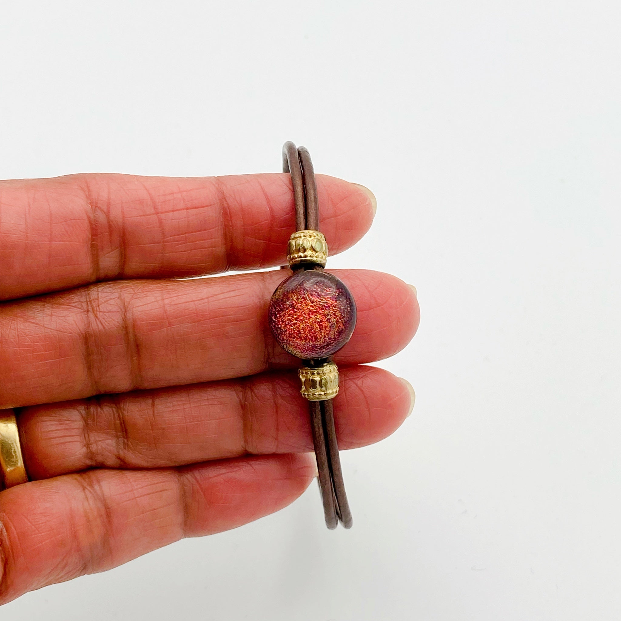 Hand holding leather bracelet with dichroic glass cabochon, by 3D Glass Designs.