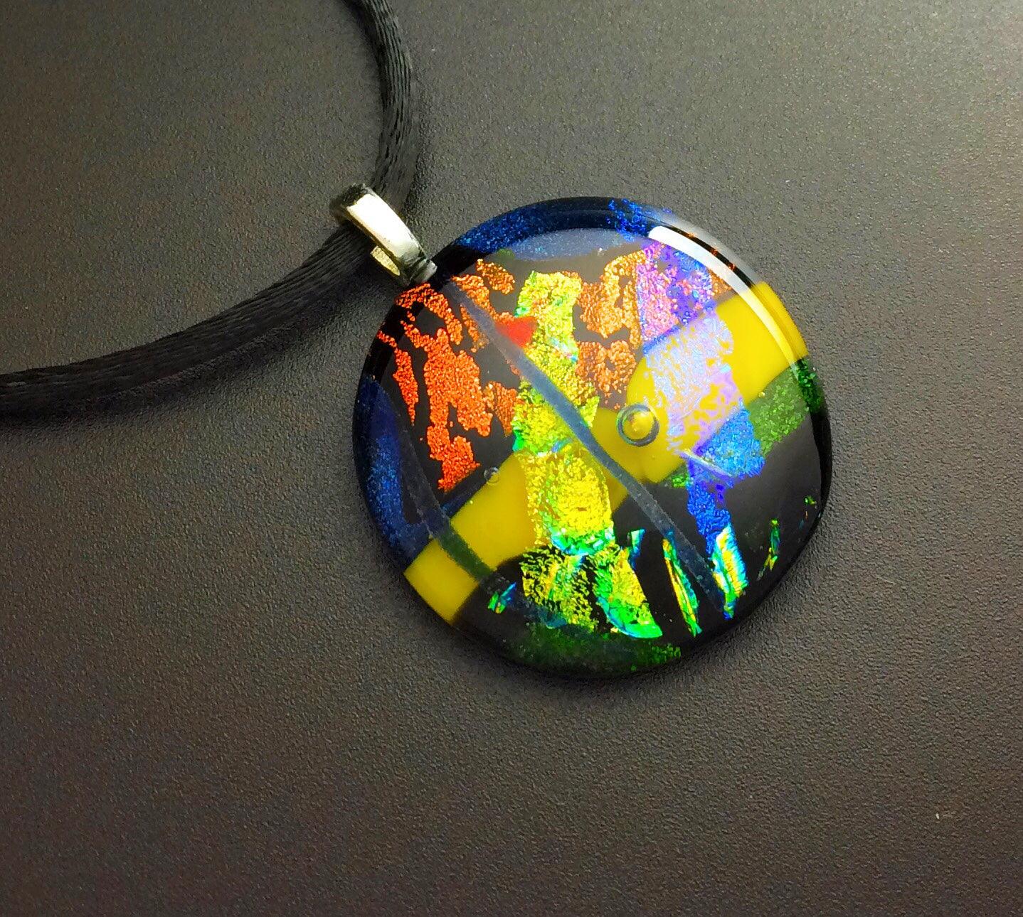 Round dichroic glass pendant necklace in green, yellow, blue, and rust hung on a 16-inch satin cord, by 3D Glass Designs.