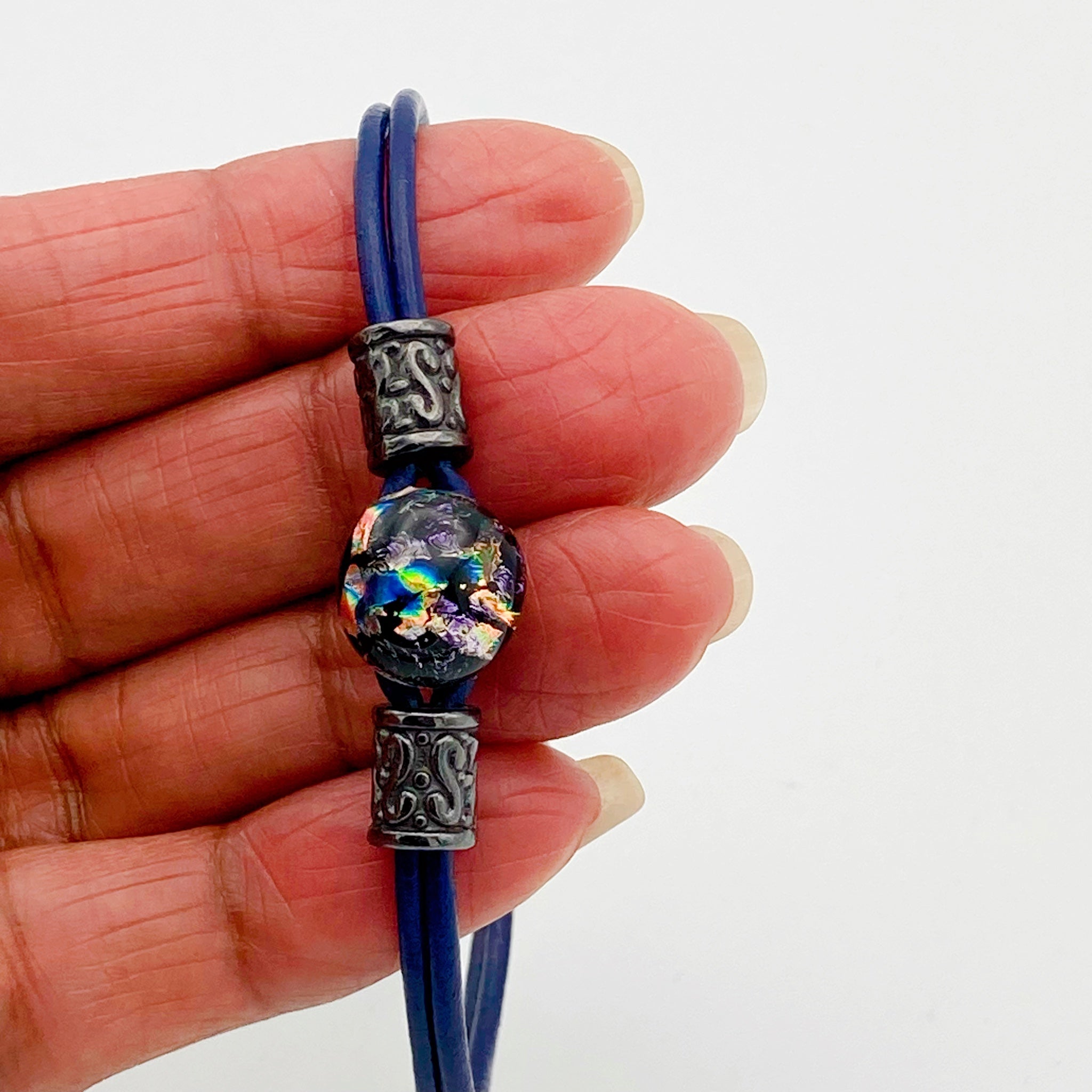 Hand holding handmade purple dichroic glass and blue leather bracelet, by 3D Glass designs.