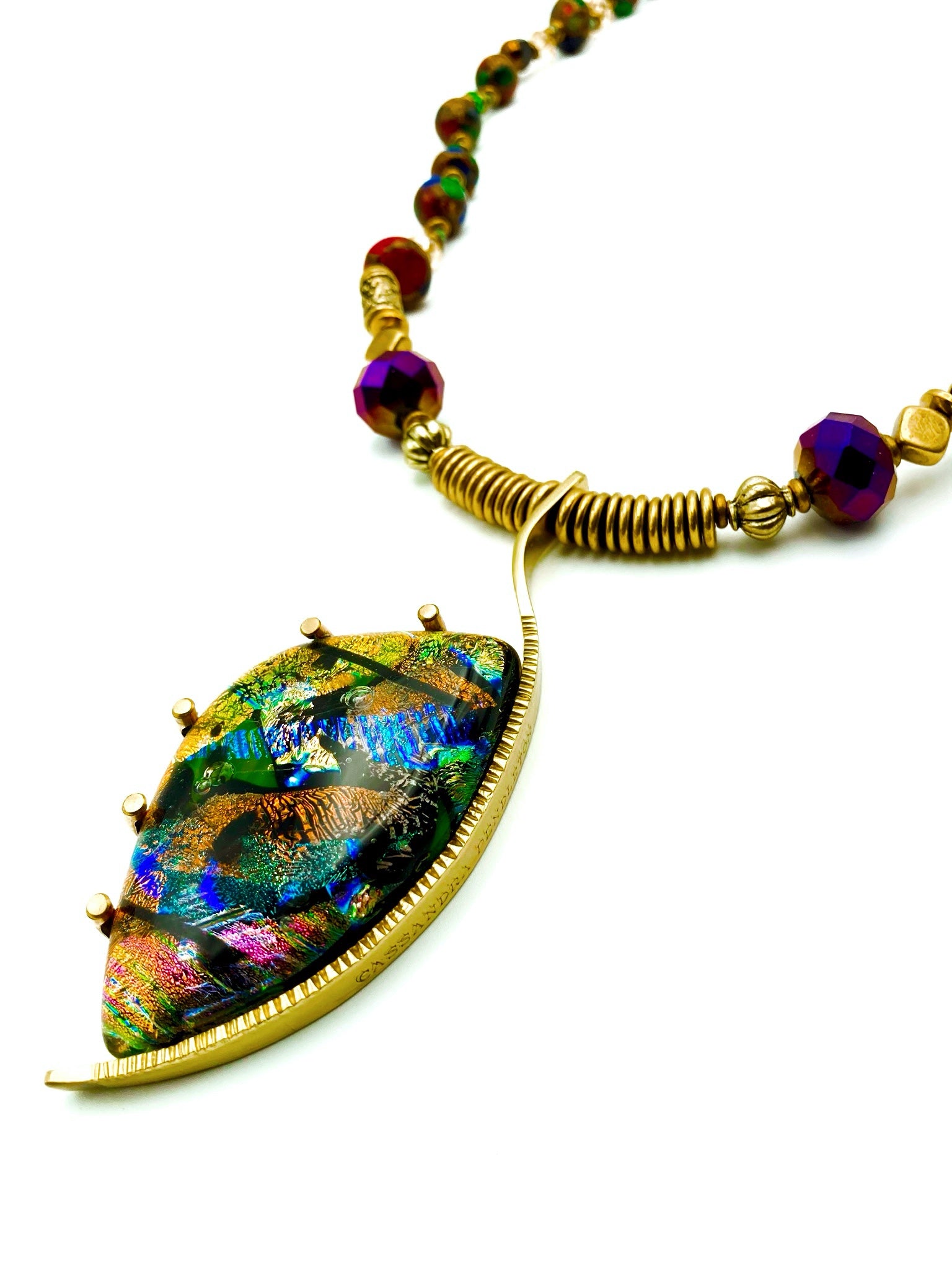 Dichroic glass set in a unique brass pendant, with prongs on left side and a textured bezel on the right side. Pendant is hung on a 29" long hand-knotted multicolor beaded necklace, by 3D Glass Designs.