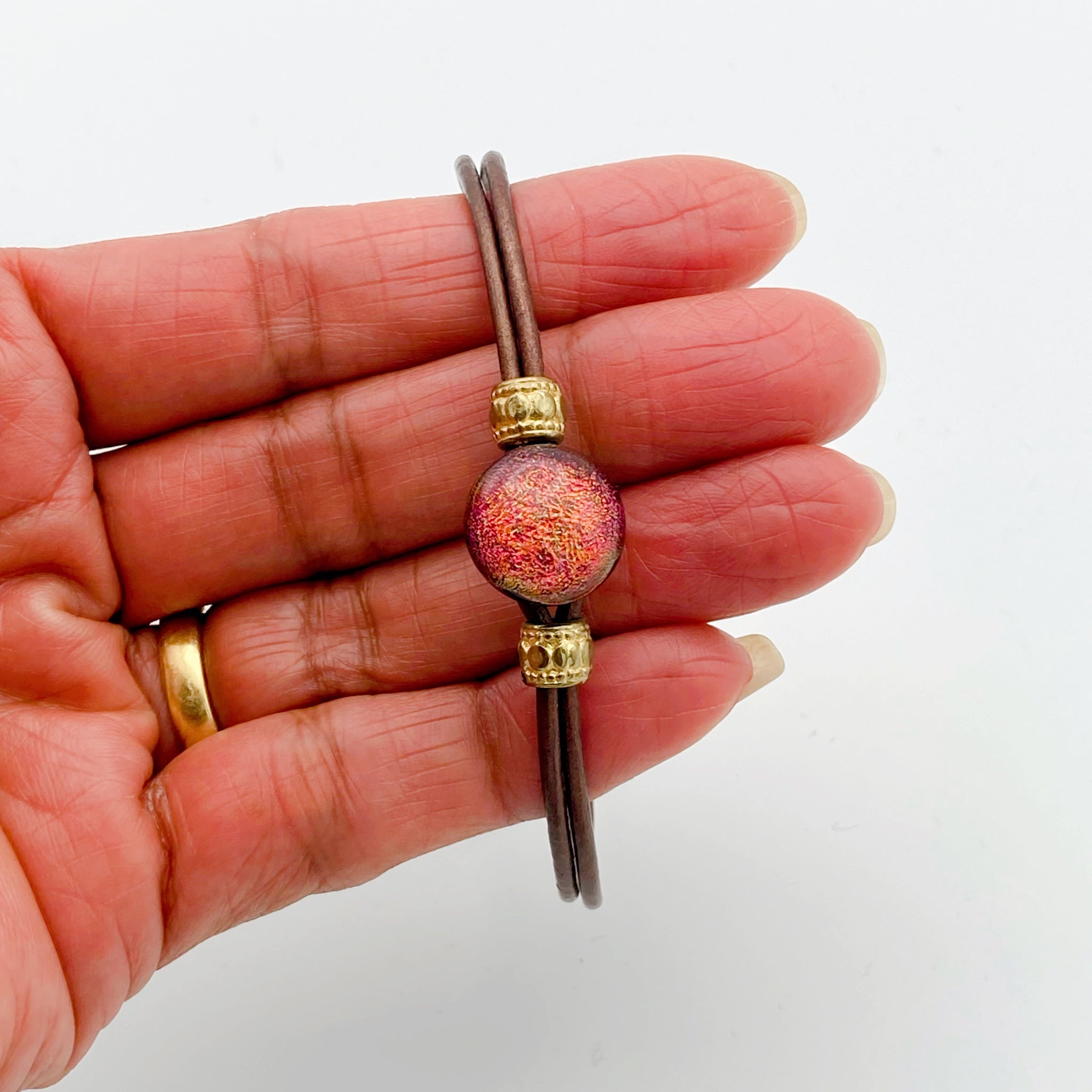 Hand holding leather bracelet with dichroic glass cabochon, by 3D Glass Designs.