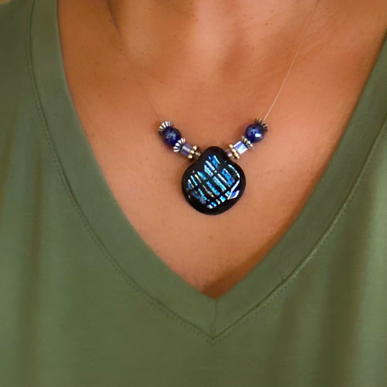 Model in a green top wearing a beaded necklace with blue striped dichroic glass pendant, by 3DGlass Designs.