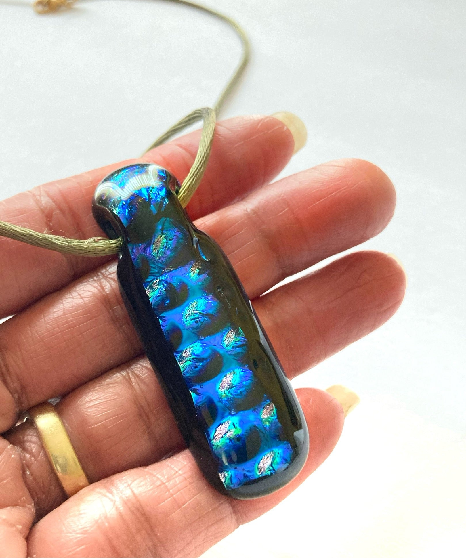 Hand holding blue and black fused glass pendant on a green satin cord, by 3D Glass Designs.