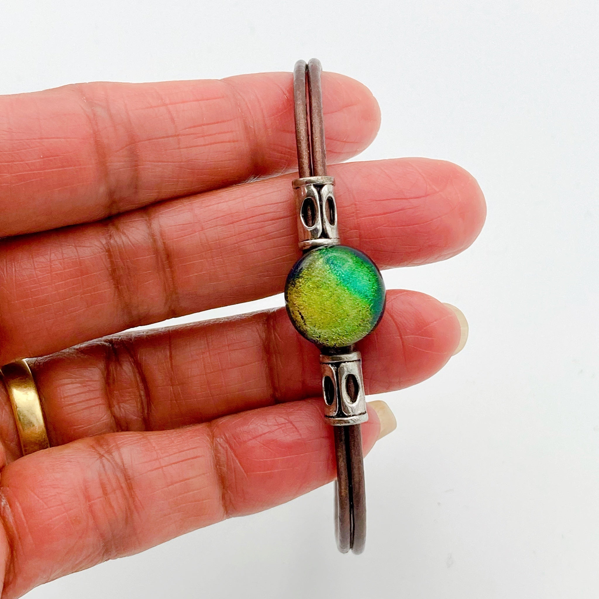 Hand holding green fused glass with metallic bronze leather cord. handmade by 3D Glass designs.