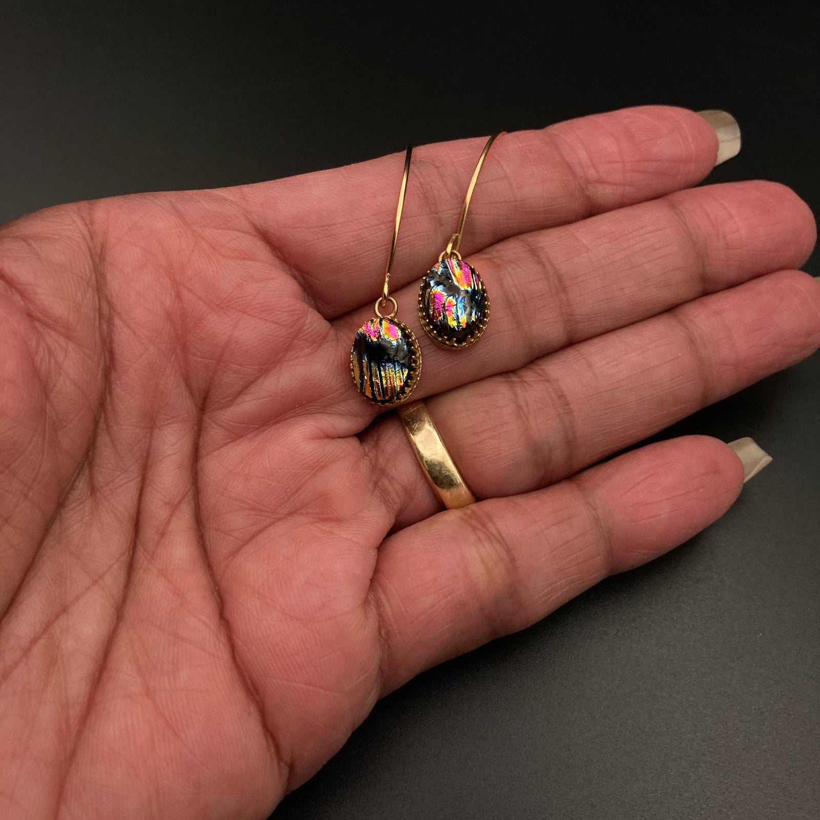 Hand holding a pair of colorful glass earrings on gold ear wires, by 3D Glass Designs.