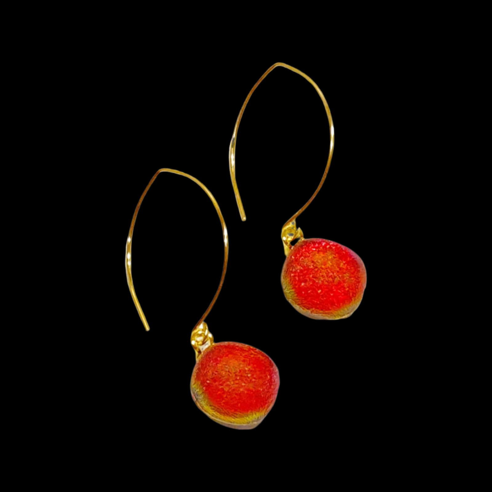 A pair of red fused glass earrings on long gold ear wires against a black background, by 3D Glass Designs.