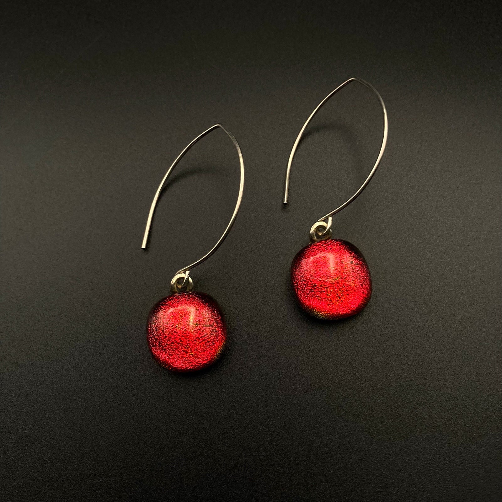 A pair of red glass dangle earrings against a grey background, by 3D Glass Designs.