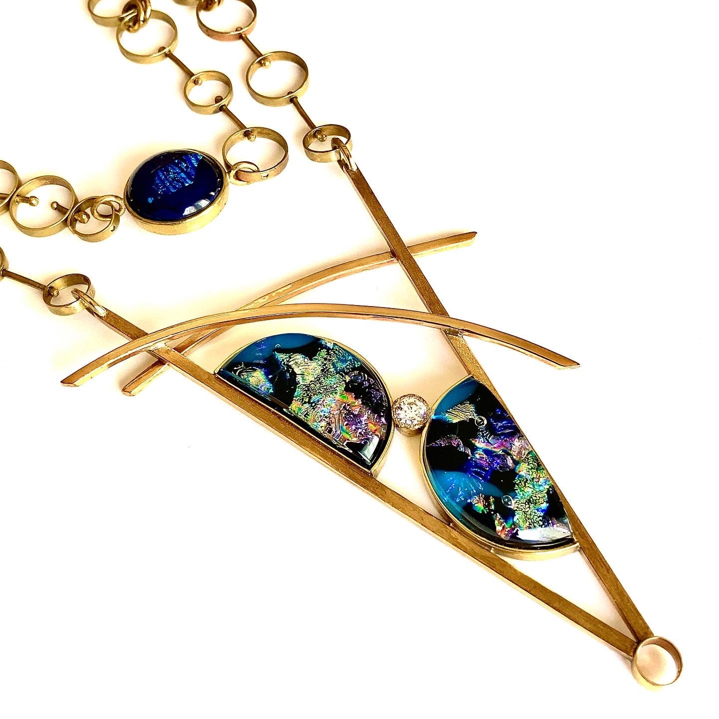 Large brass pendant with  teal, green and purple fused glass, geometric inspired with two semi-circles and CZ framed in a V, with two slightly curved arch's above. Chain made of various size circles linked together with a fused glass clasp, By 3D Glass Designs. 