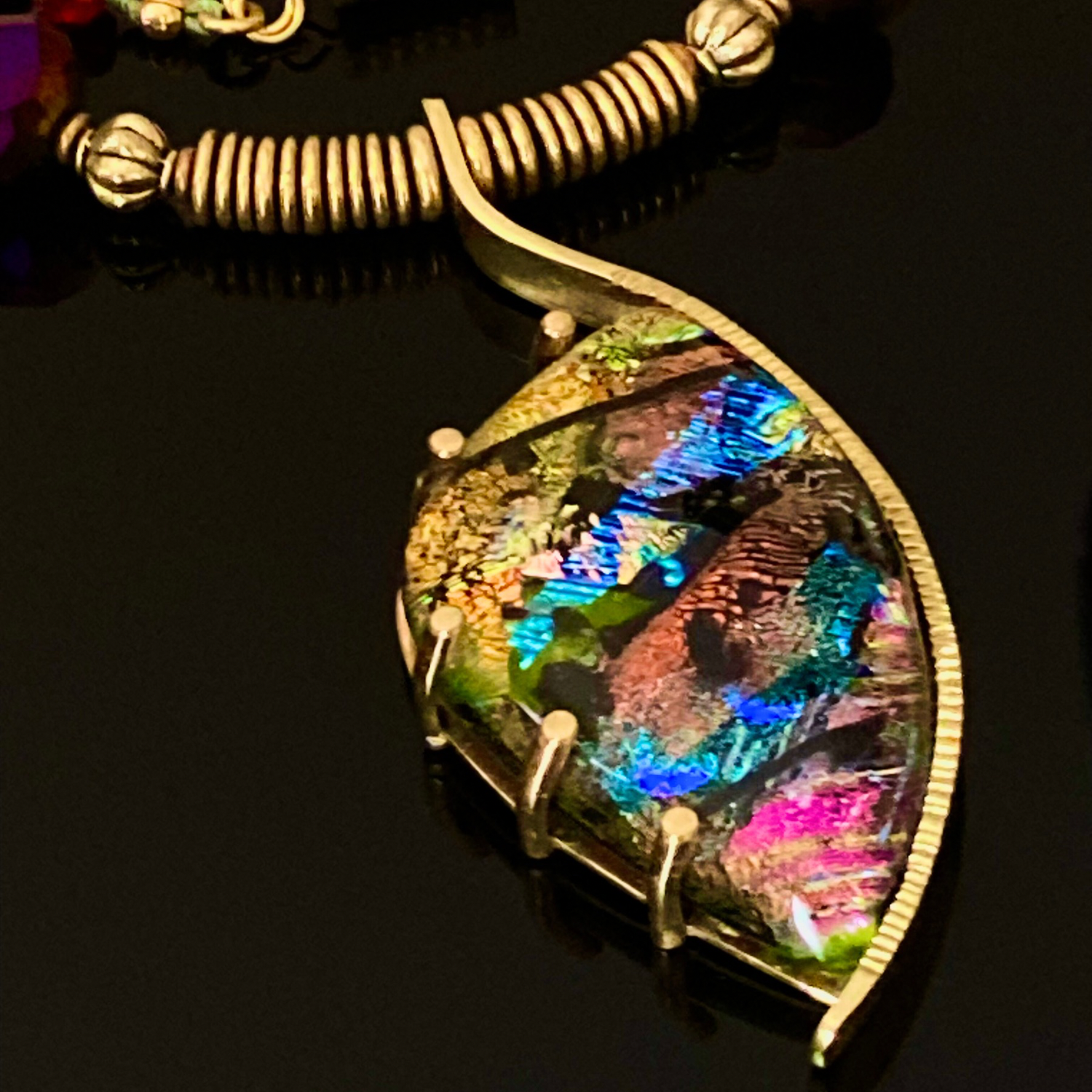 Dichroic glass set in a unique brass pendant, with prongs on left side and a textured bezel on the right side. Pendant is hung on a 29" long hand-knotted multicolor beaded necklace, by 3D Glass Designs.