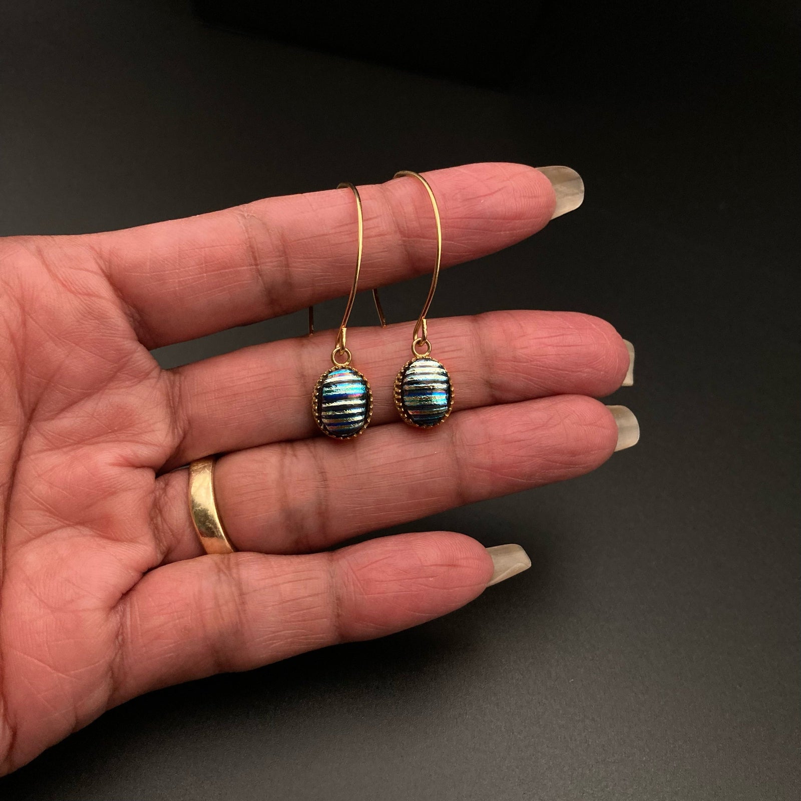 Hand holding blue striped earrings with long gold-plated ear wires, by 3D Glass Designs.