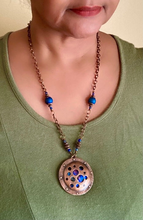 Model wearing round copper and dichroic glass pendant on a beaded copper chain, by 3D Glass Designs.