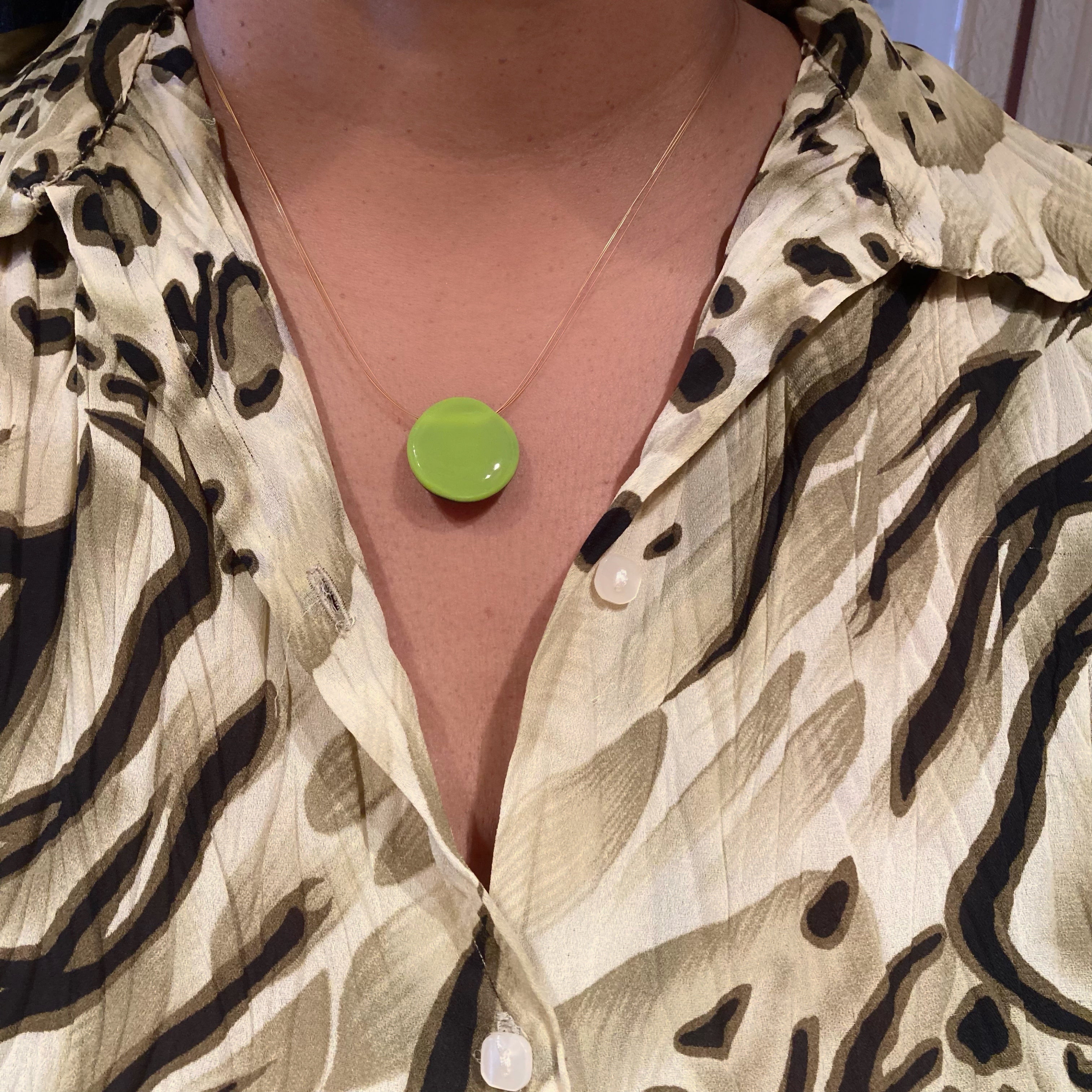 Model wearing a small lime green round glass pendant on three gold cords, by 3D Glass Designs. 
