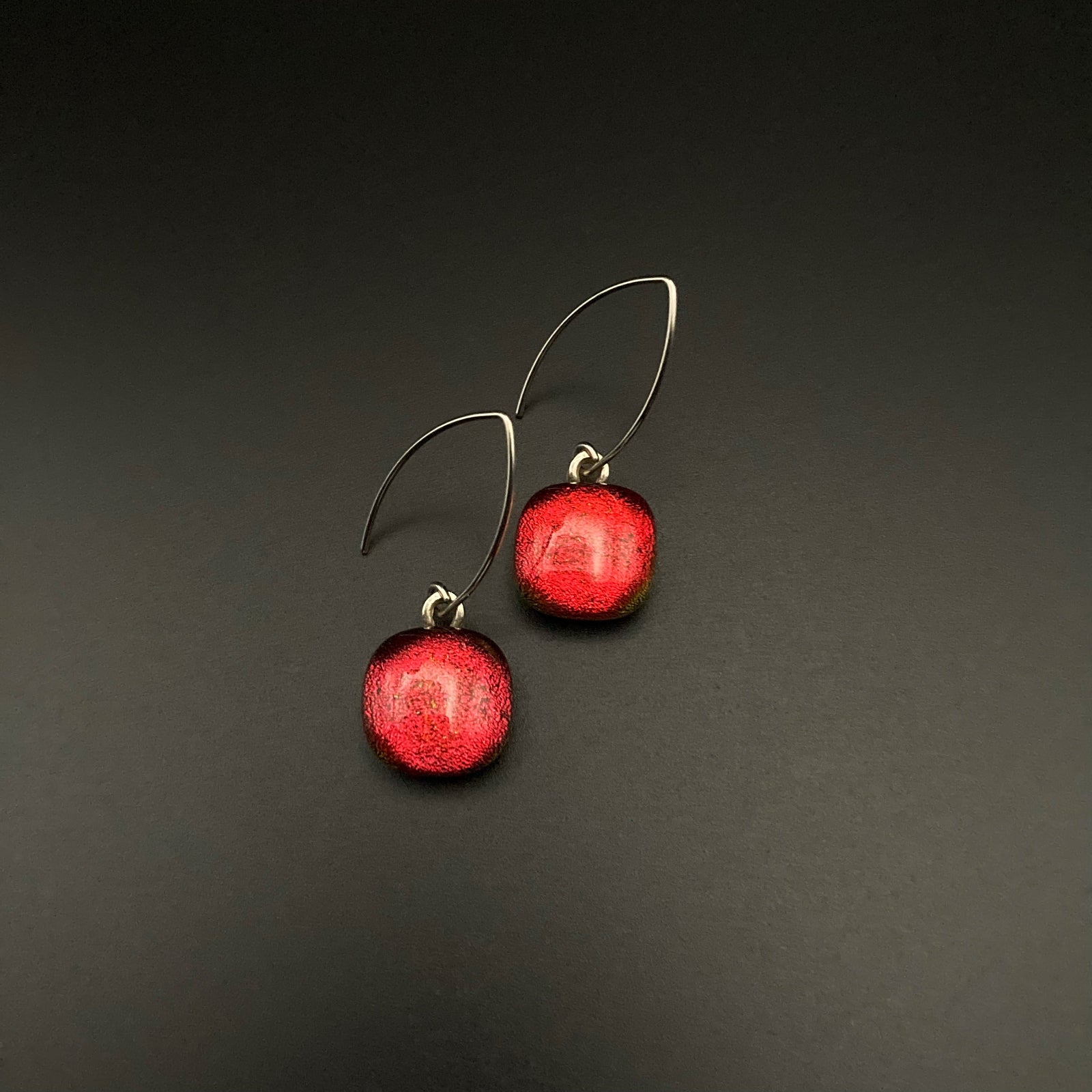 A pair of red fused glass earrings on a grey background, by 3D Glass Designs.