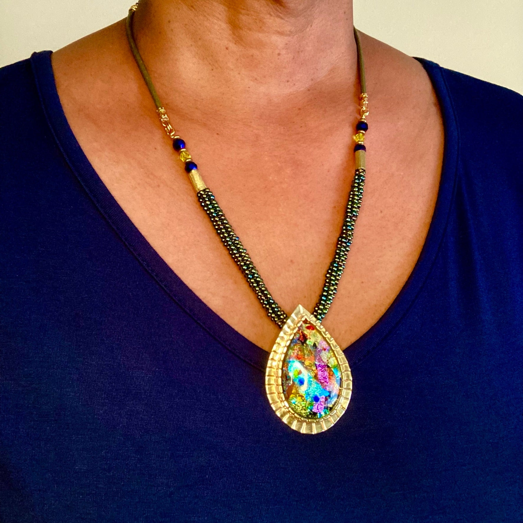Model wearing colorful dichroic glass statement necklace with large teardrop shaped pendant and beaded necklace. By 3D Glass Designs. 