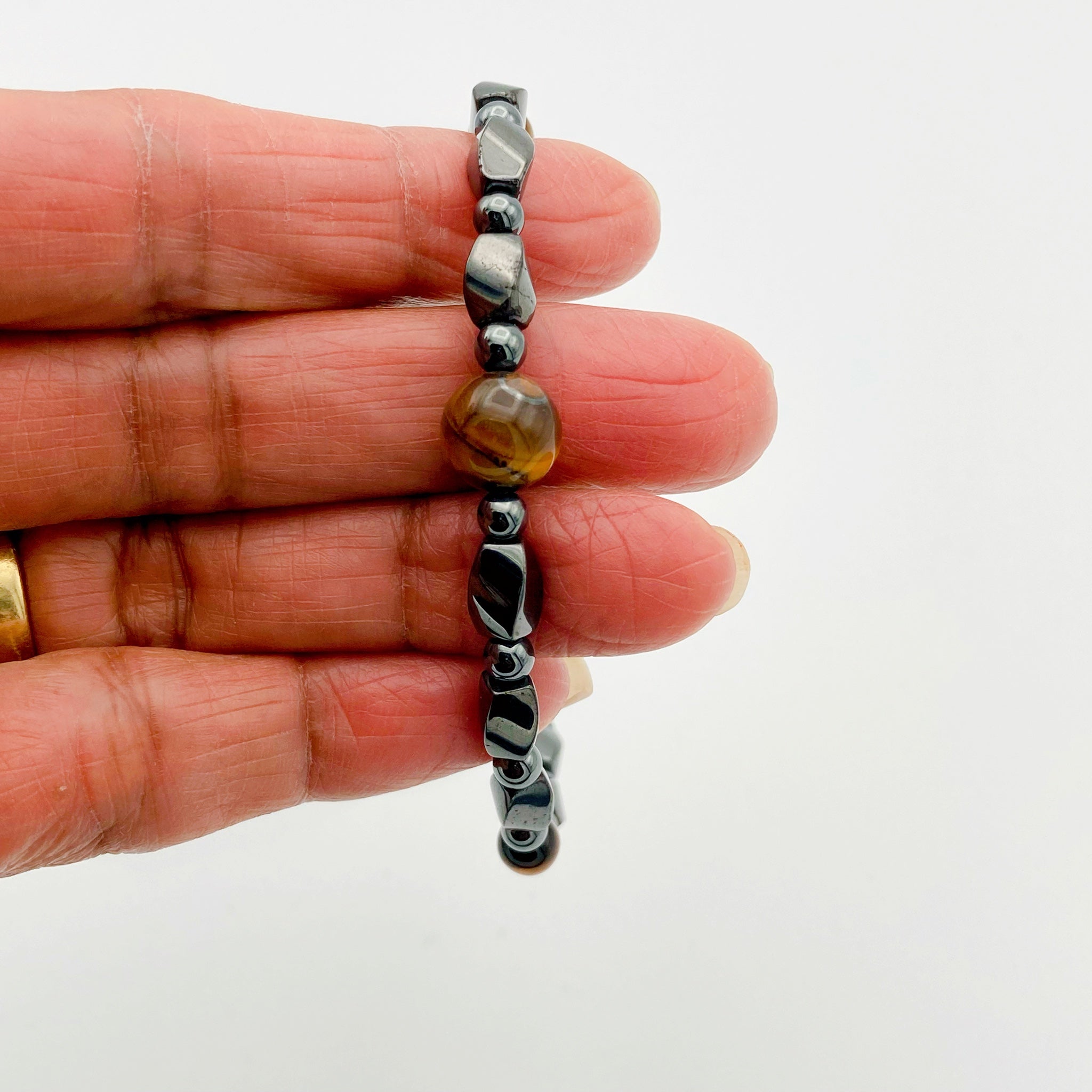 Hand holding Unisex Hematite and tiger's eye beaded bracelet, by 3D Glass Designs.